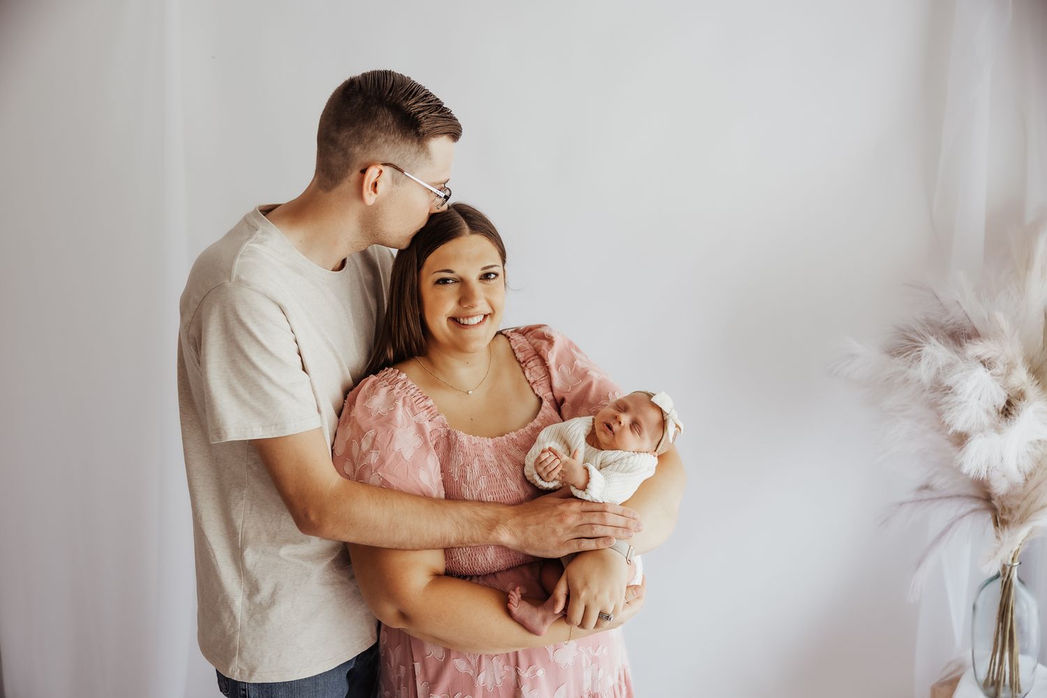 Young couple smiling and holding their newborn baby in a bright studio setting.