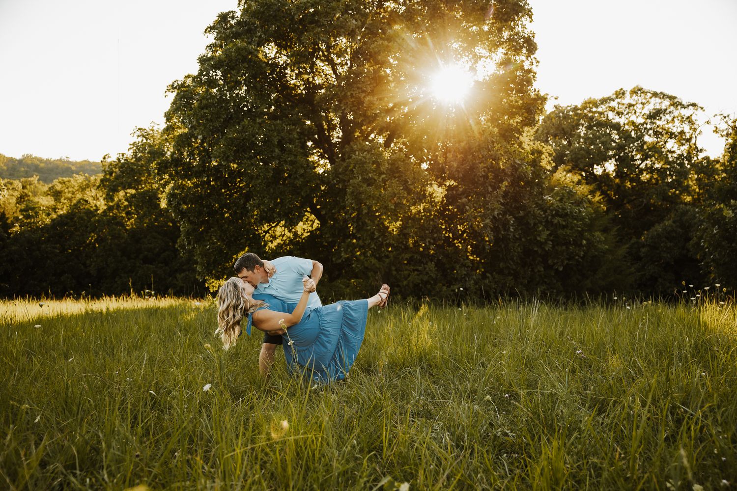 Couple kissing in a sunlit meadow, during golden hour sunlight through trees in Kansas.