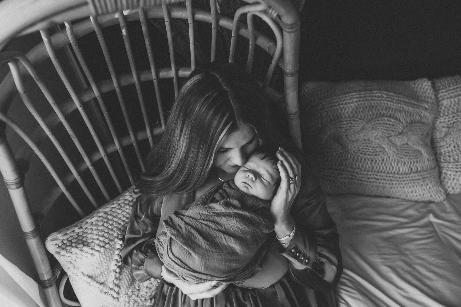 Black and white photo of a mother tenderly holding her newborn baby while sitting in a rocking chair.