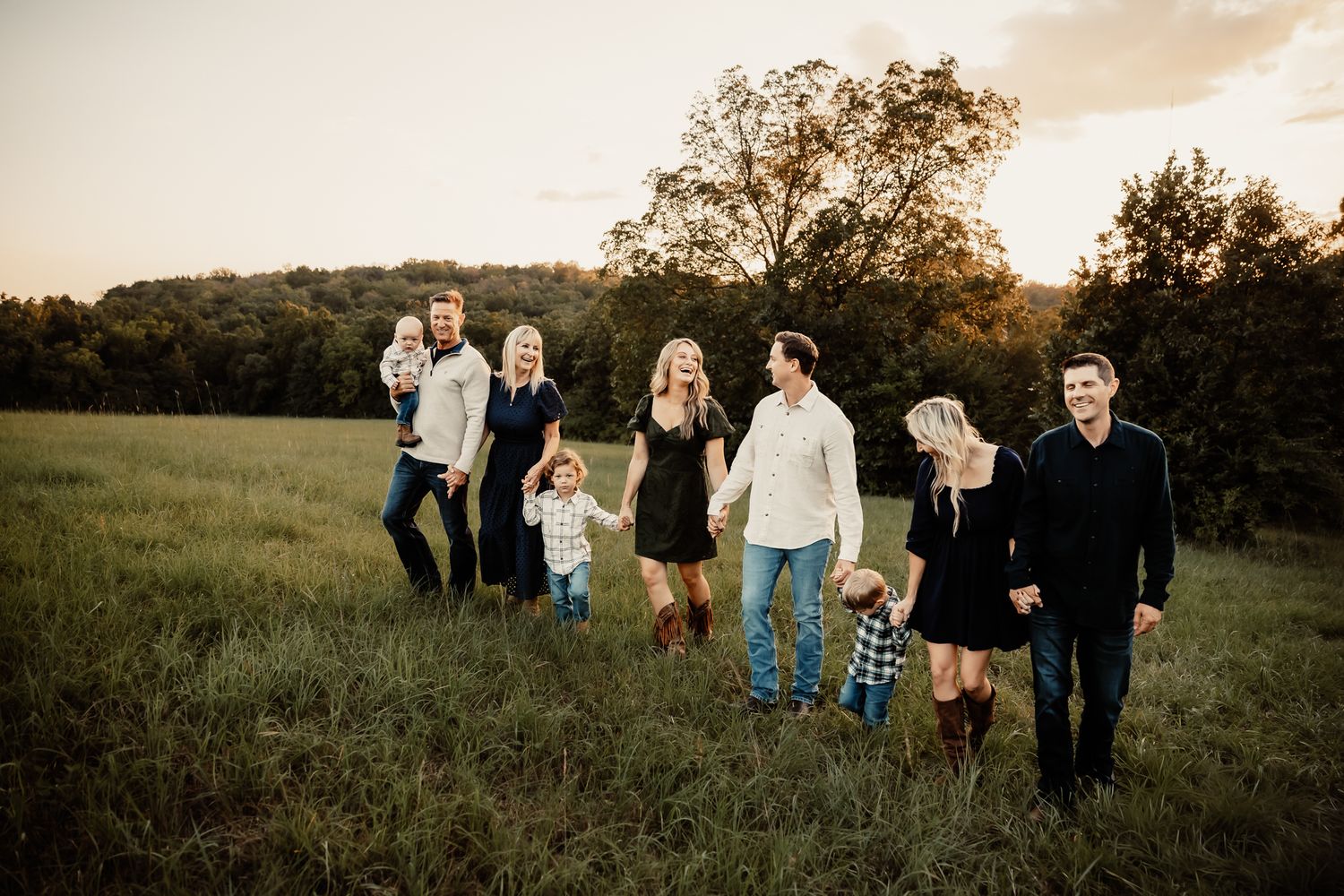 Large family walking together in a green meadow at golden hour sunset, multi-generational outdoor portrait.