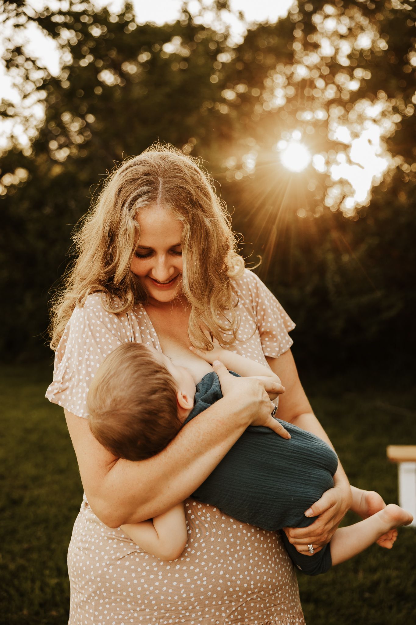 Mother smiling while holding her baby in golden sunset light in an outdoor garden setting.