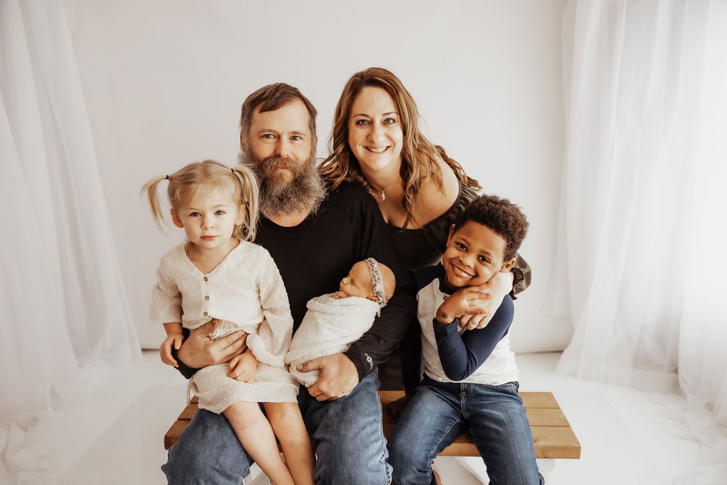 Happy family of five posing together, parents with three young children including a newborn, in a bright studio setting.