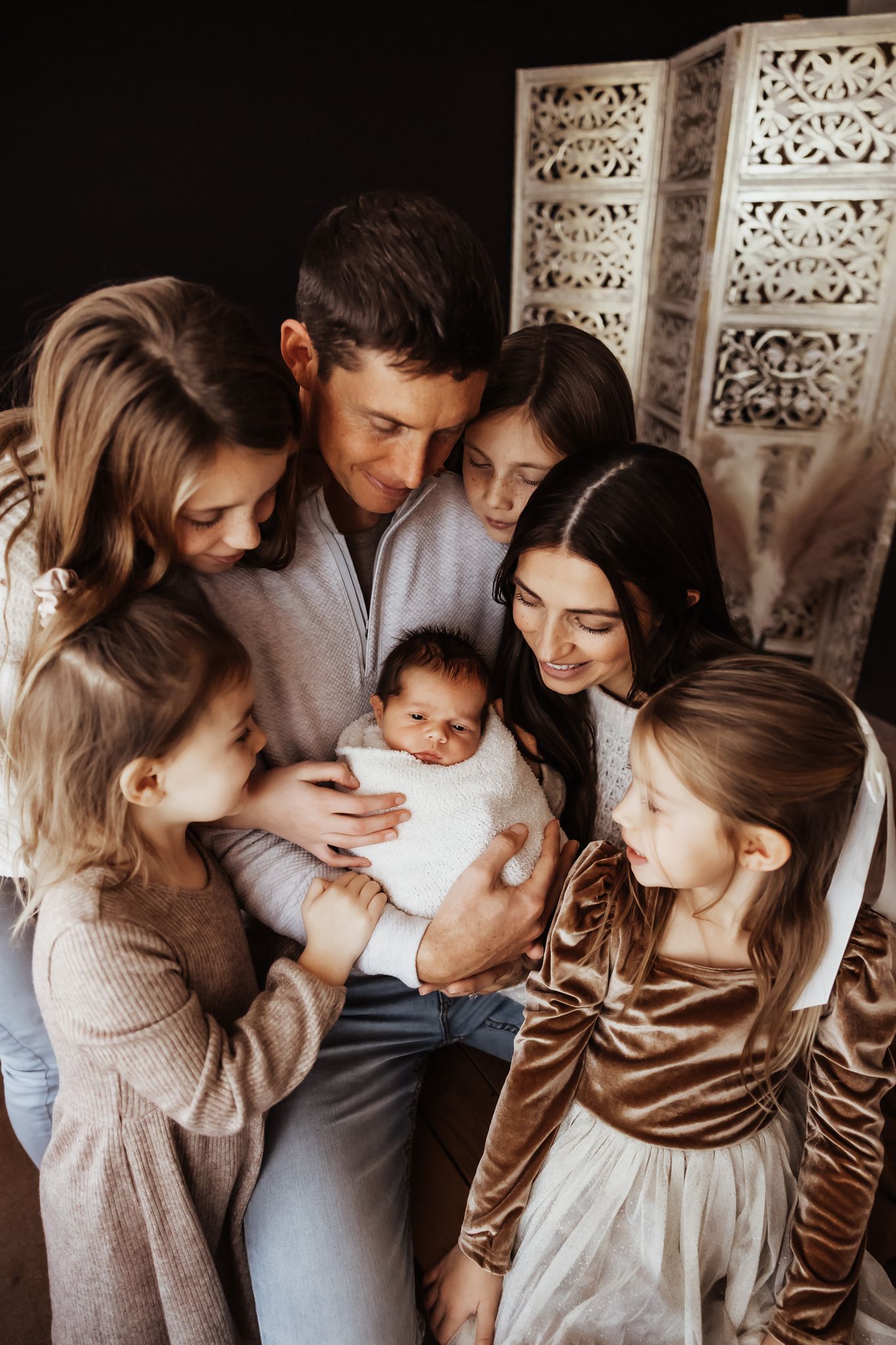 A loving family gathers closely around a newborn baby, with parents and four children sharing a tender moment together. Topeka, KS
