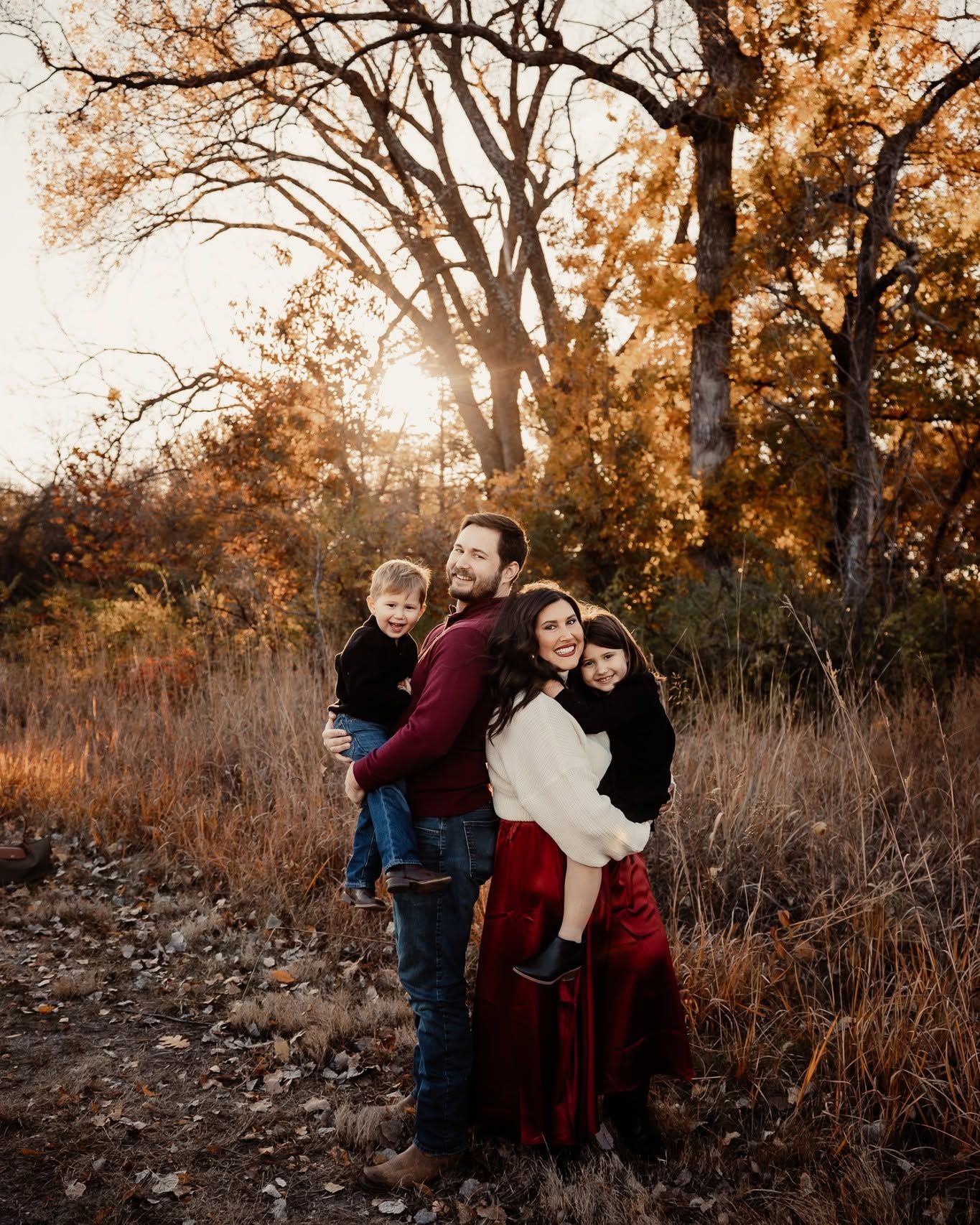 Happy family of four posing together in autumn forest with warm golden sunset background.