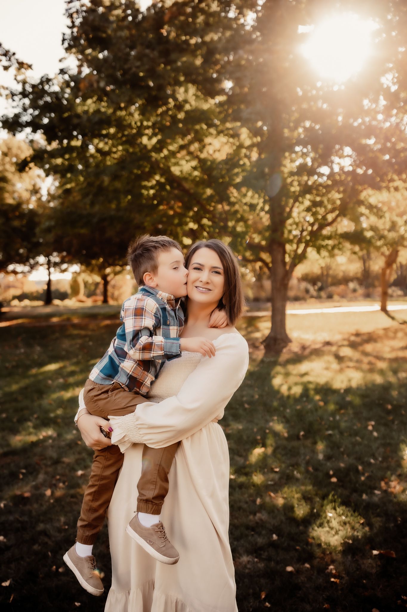 A mother holds her young son as he kisses her cheek during a golden hour outdoor photo session.
