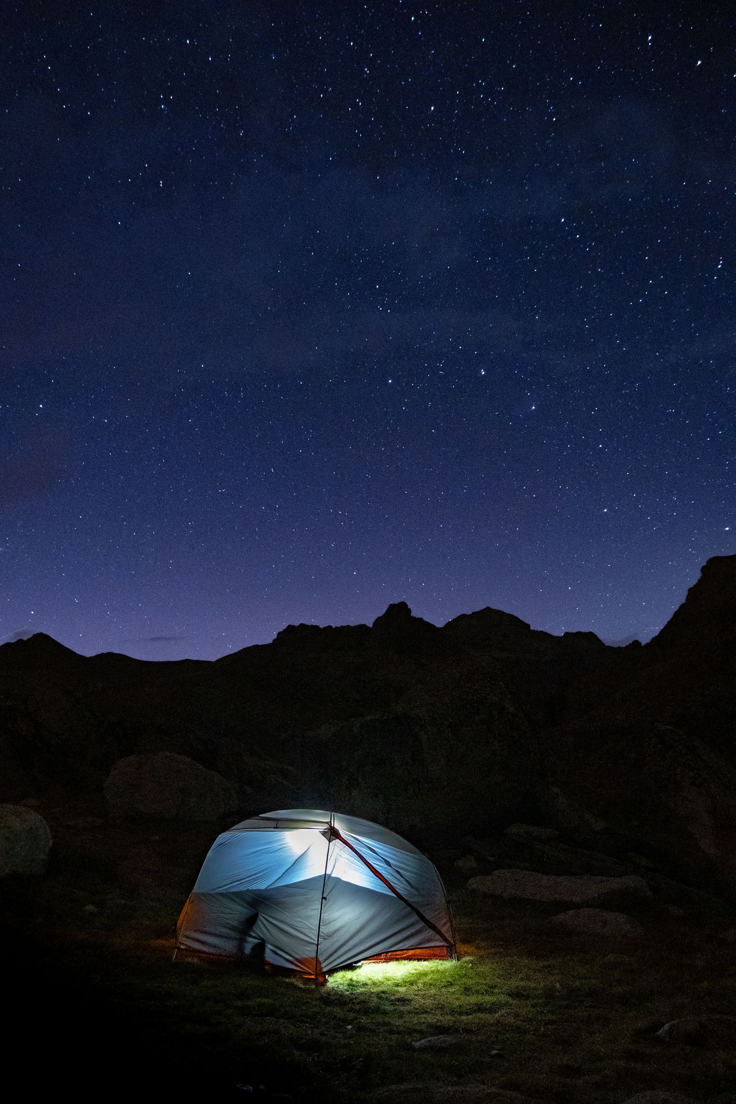 Photo de nuit d'un paysage en montagne dans les Alpes, une tente éclairée, et un ciel étoilé