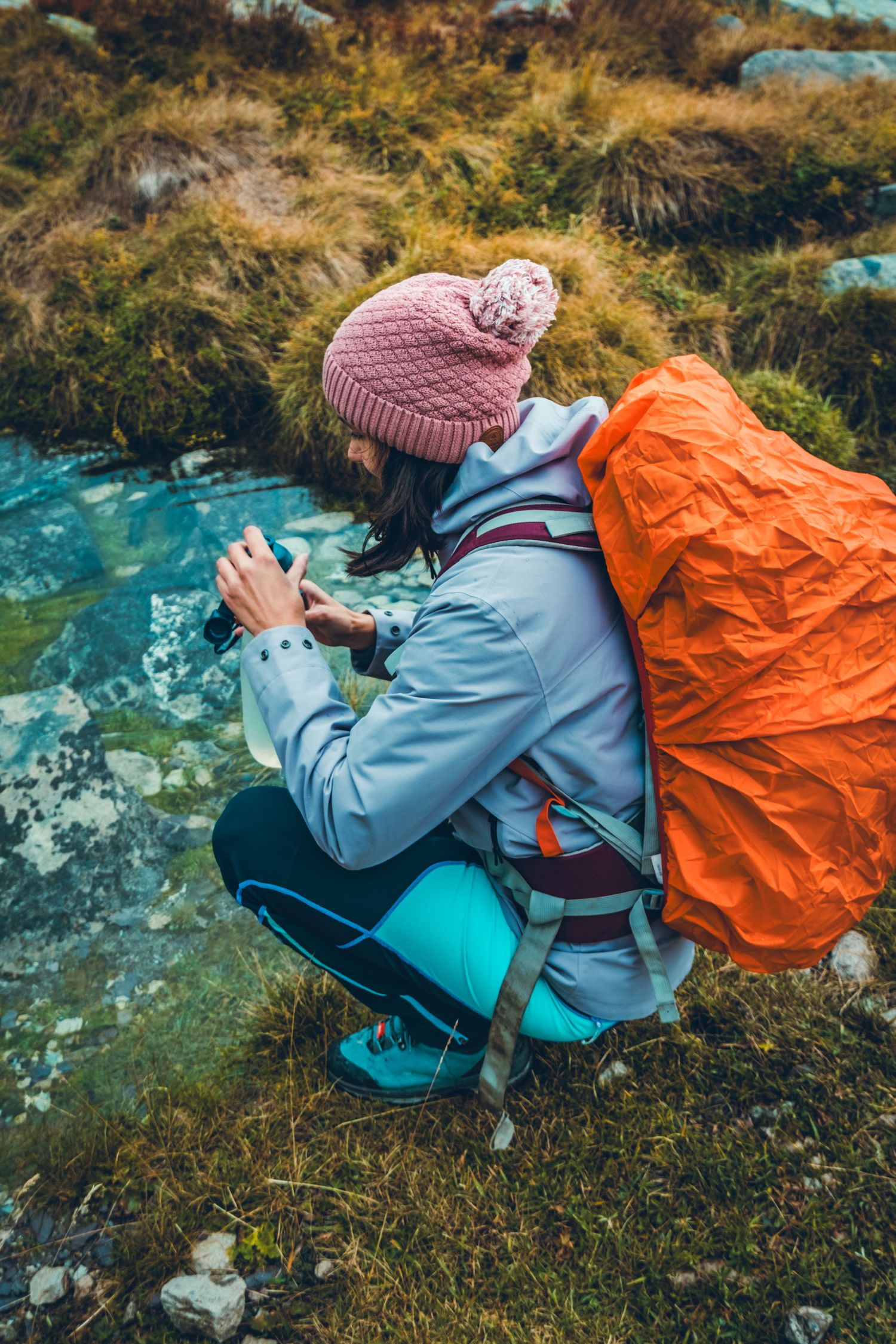 Photo d'une femme randonneuse en bonnet qui remplit sa gourde d'eau dans un lac