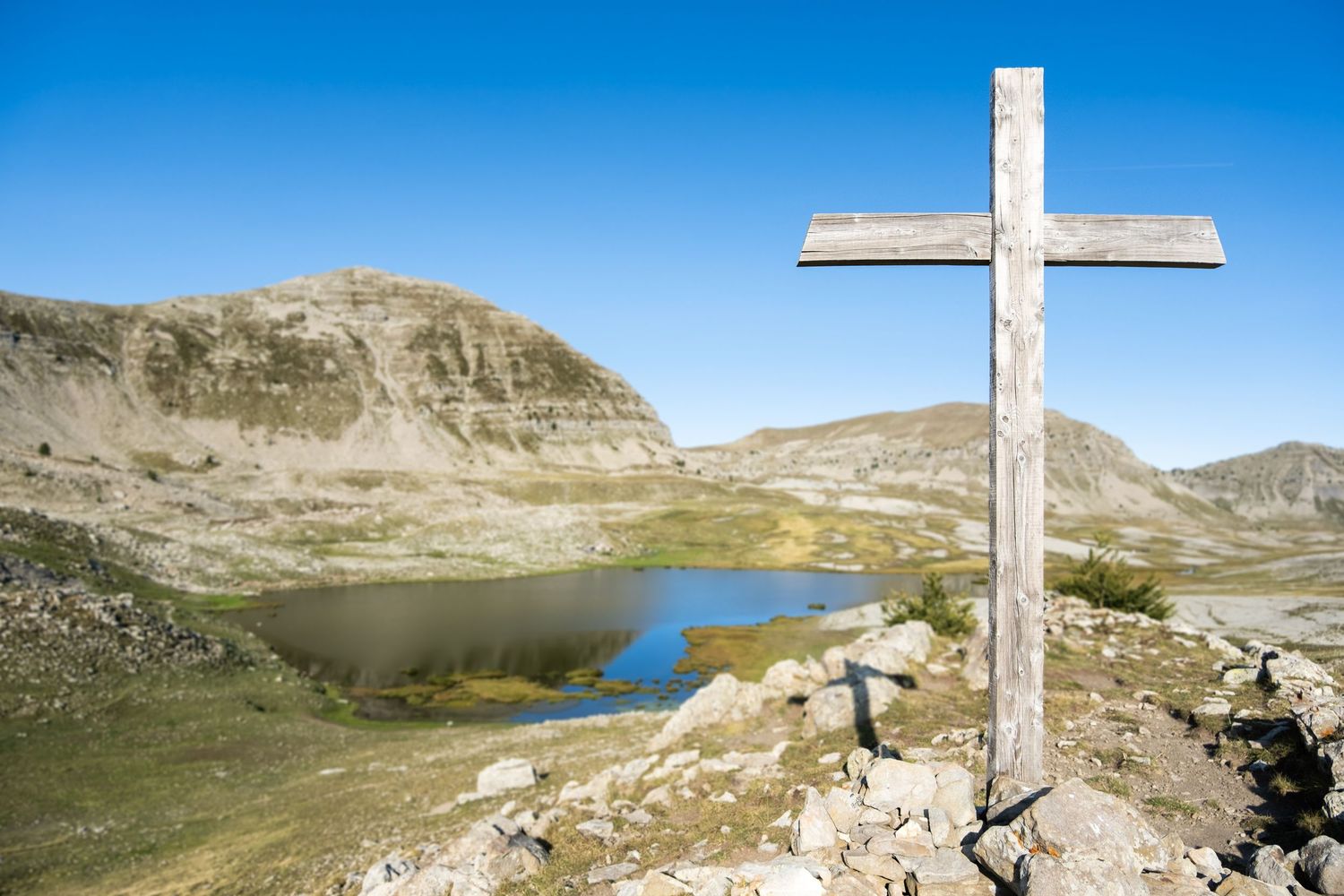 Photo de paysage dans les Alpes, avec une croix en bois devant un lac