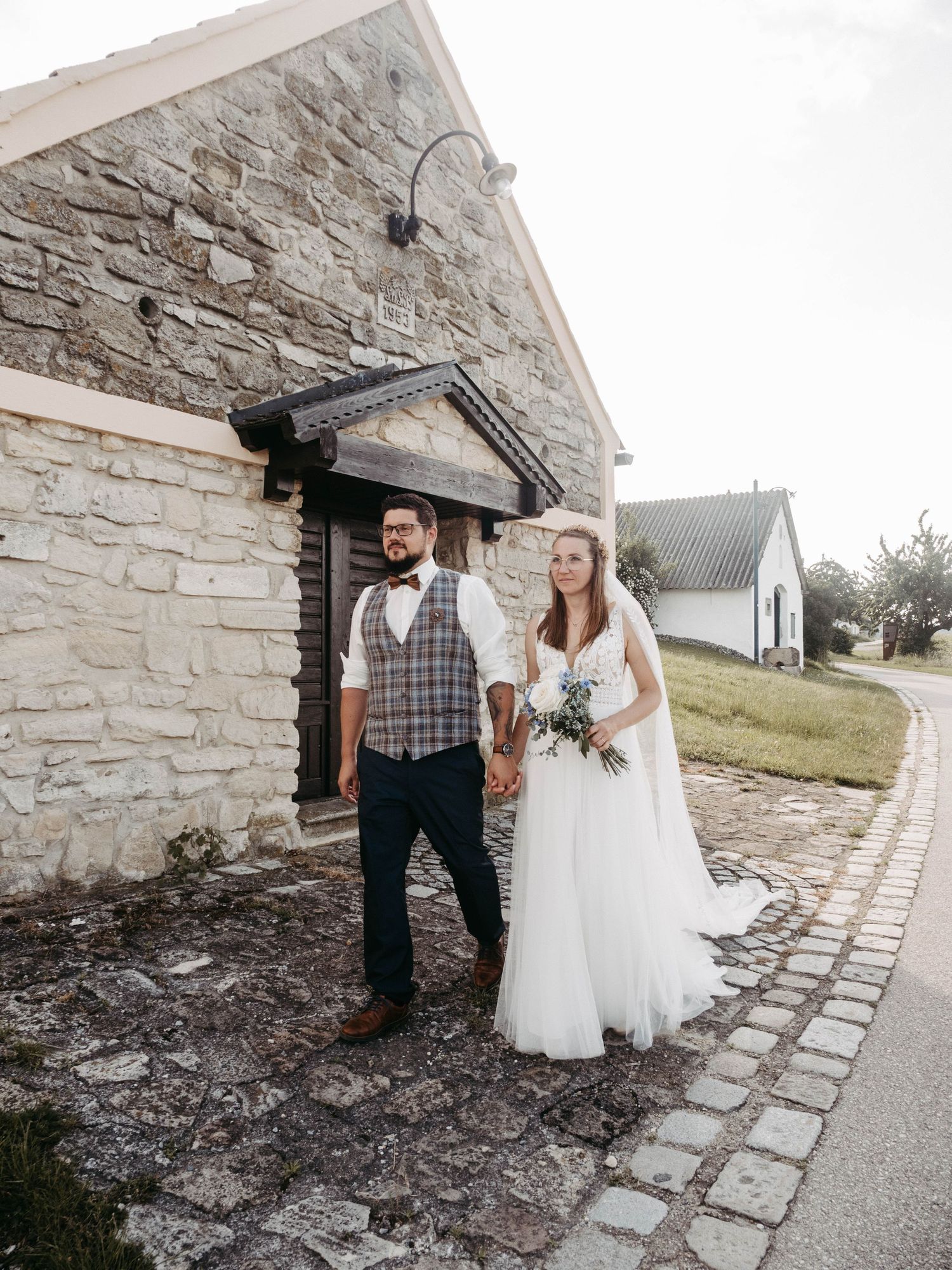 Bride and groom holding hands outside a rustic stone building on their wedding day.