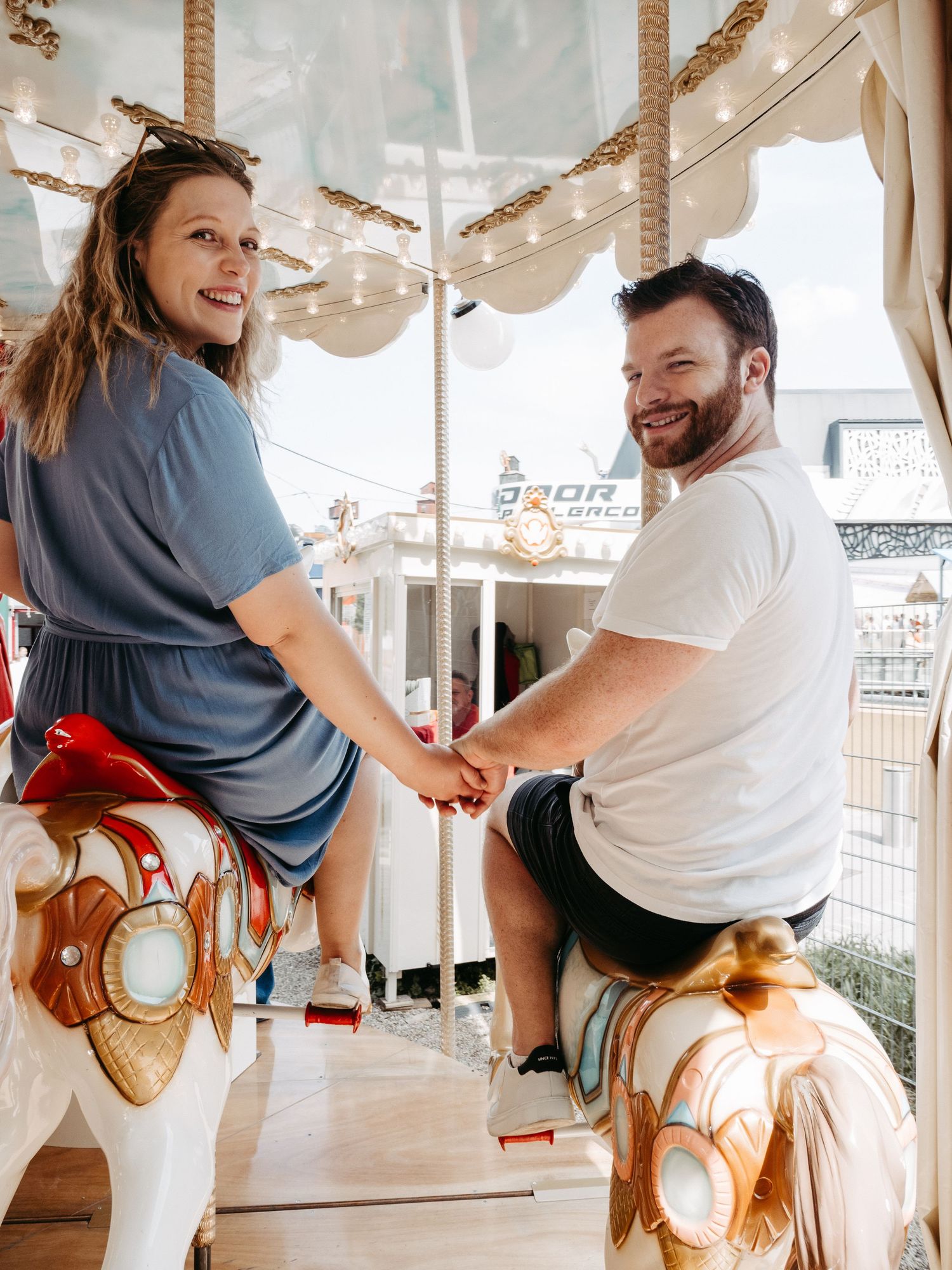 Playful carousel engagement photoshoot with couple enjoying sweet moments on vintage fairground ride.