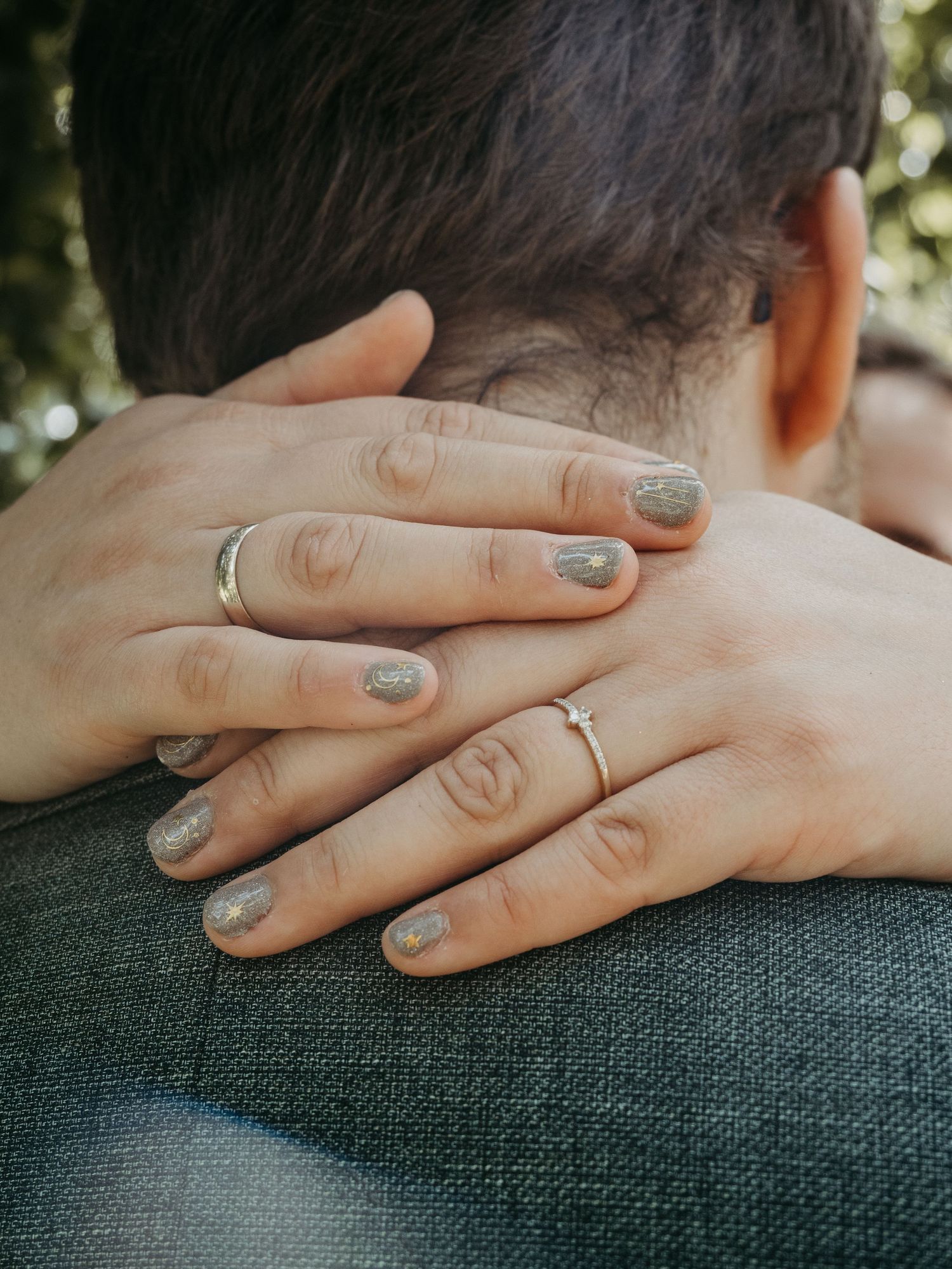 Close-up of couple's hands showing wedding rings, with glittery gray nail polish, embracing tenderly.