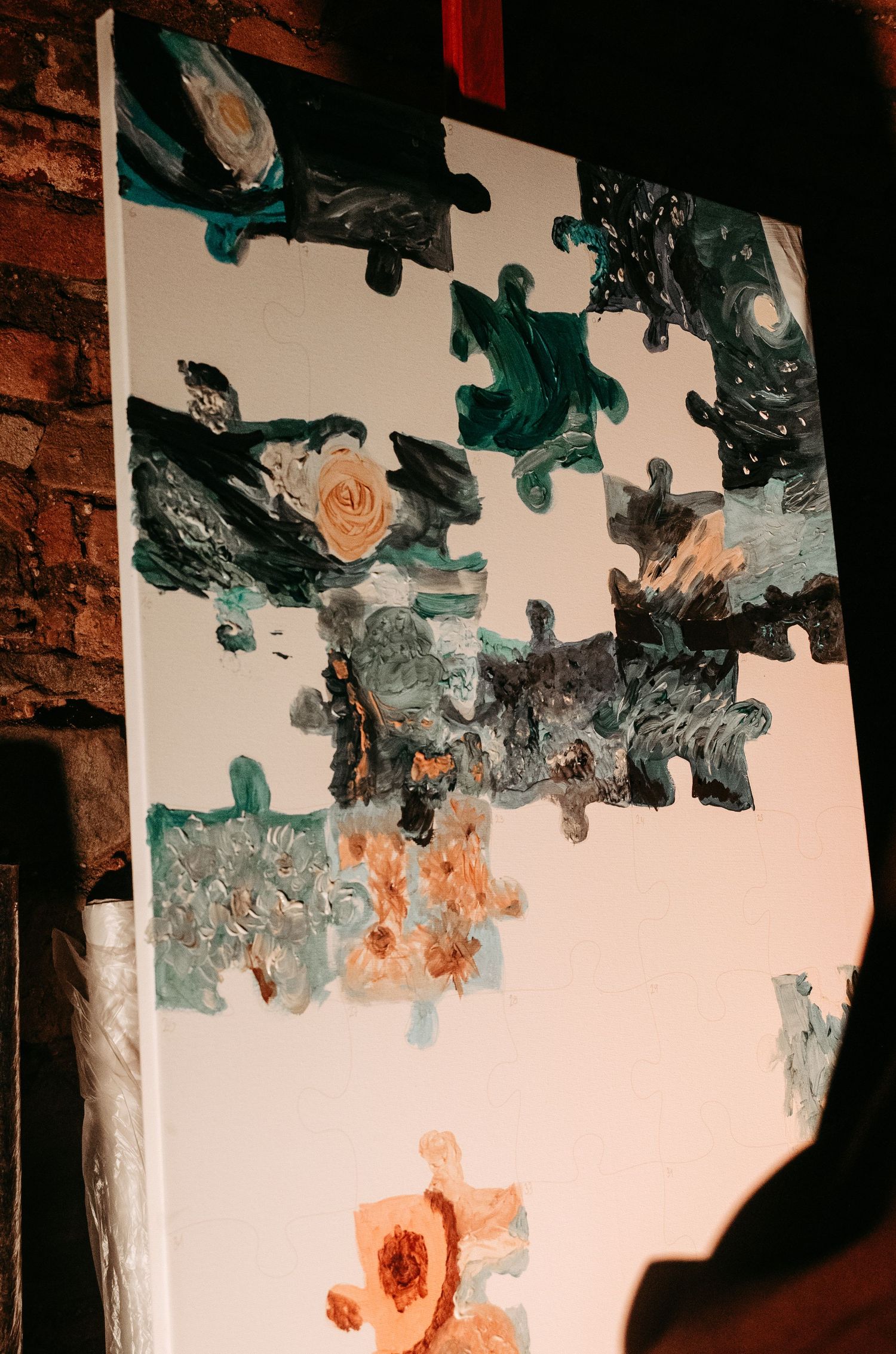 Abstract painted puzzle canvas artwork displayed against brick wall at wedding reception.