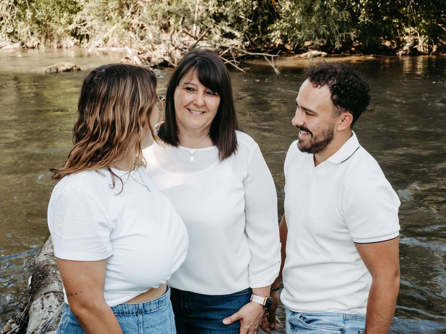 Group sitting by riverside sharing casual moments in white t-shirts.