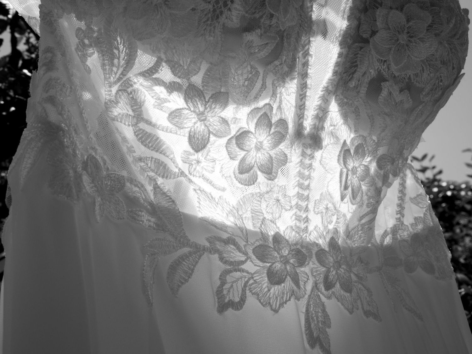 Black and white close-up of an elegant wedding dress featuring intricate floral lace embroidery detailing.