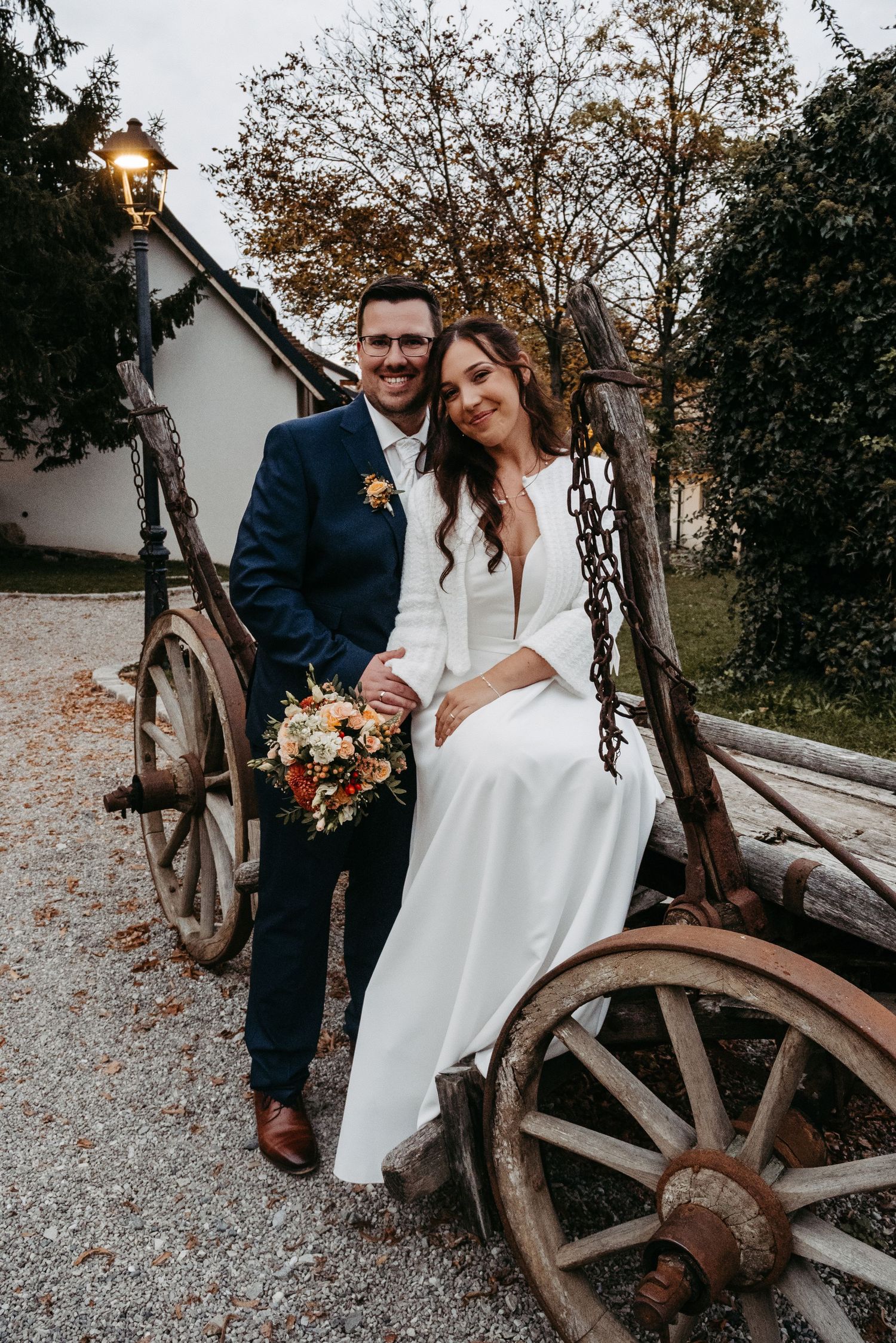 Bride and groom posing together on vintage wooden wagon at fall wedding.