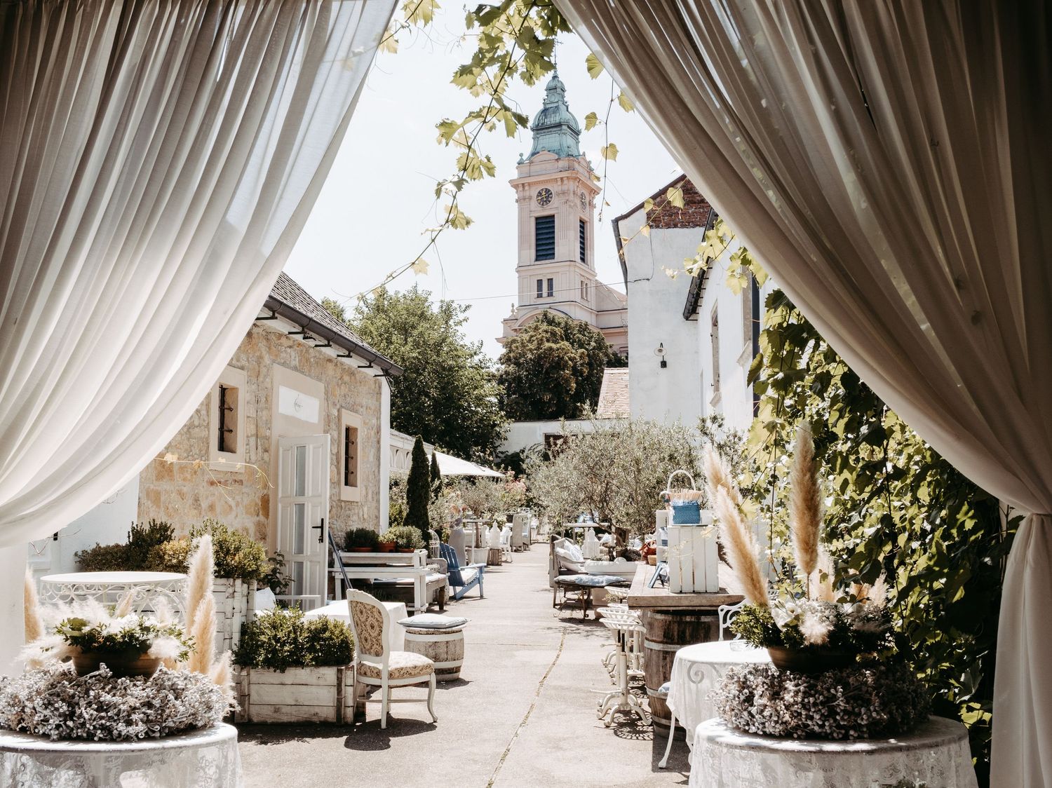 Outdoor wedding venue with flowing white curtains and garden view through draped archways.