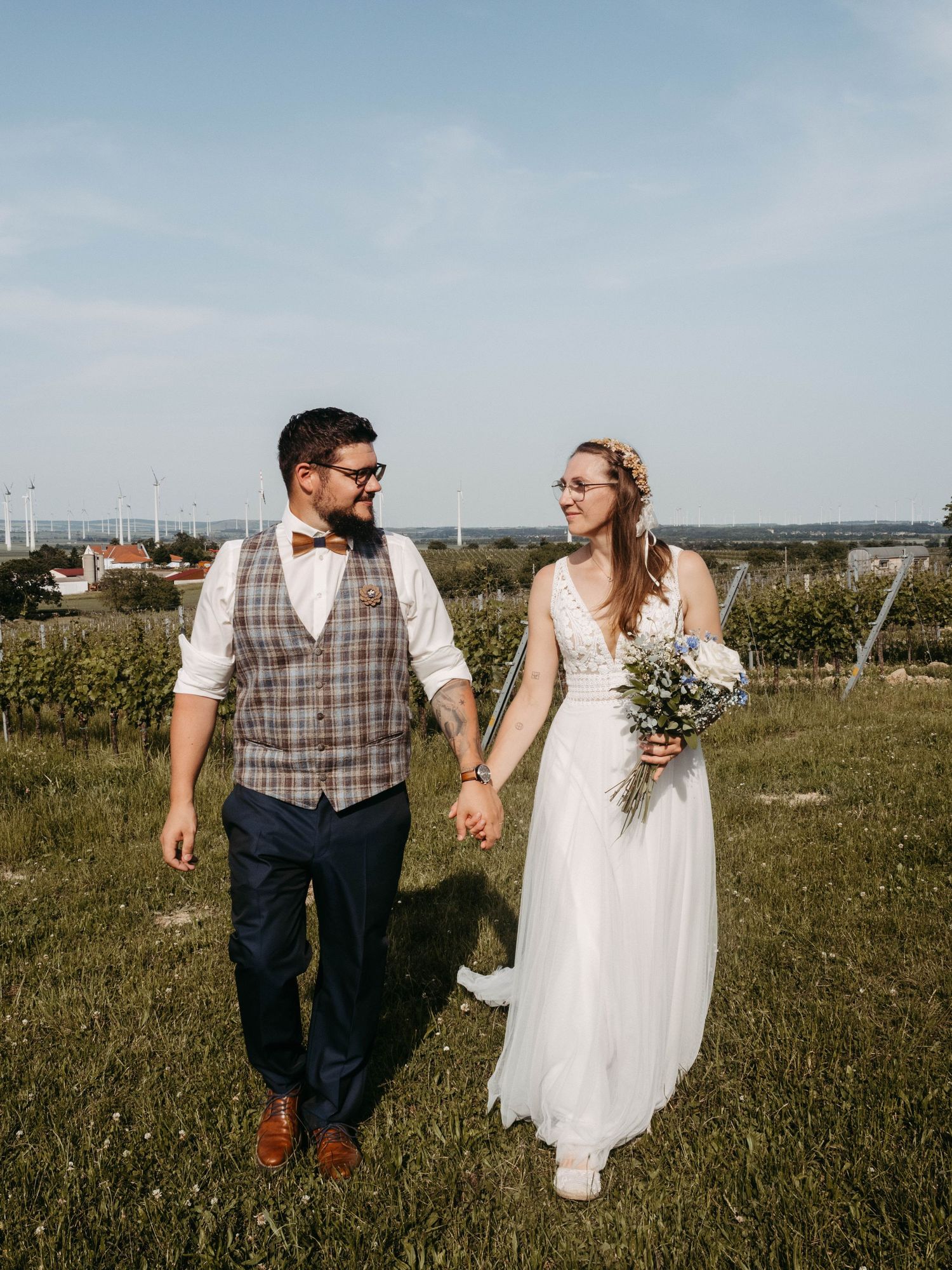 Newlyweds walking together in grassy field with bride holding floral bouquet.