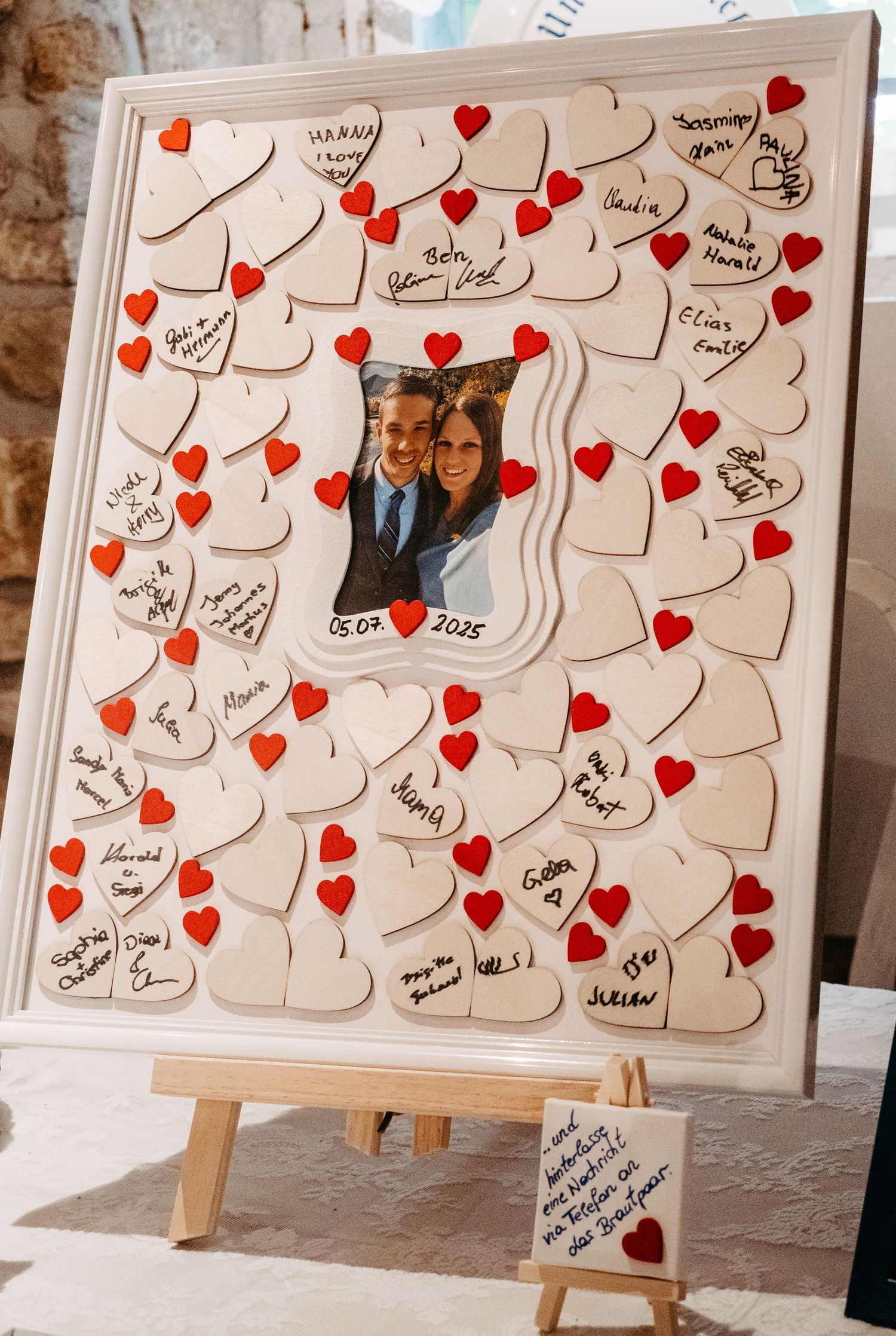 Wedding guest book frame with signed hearts and couple photo dated 05.04.2025 displayed on an easel.