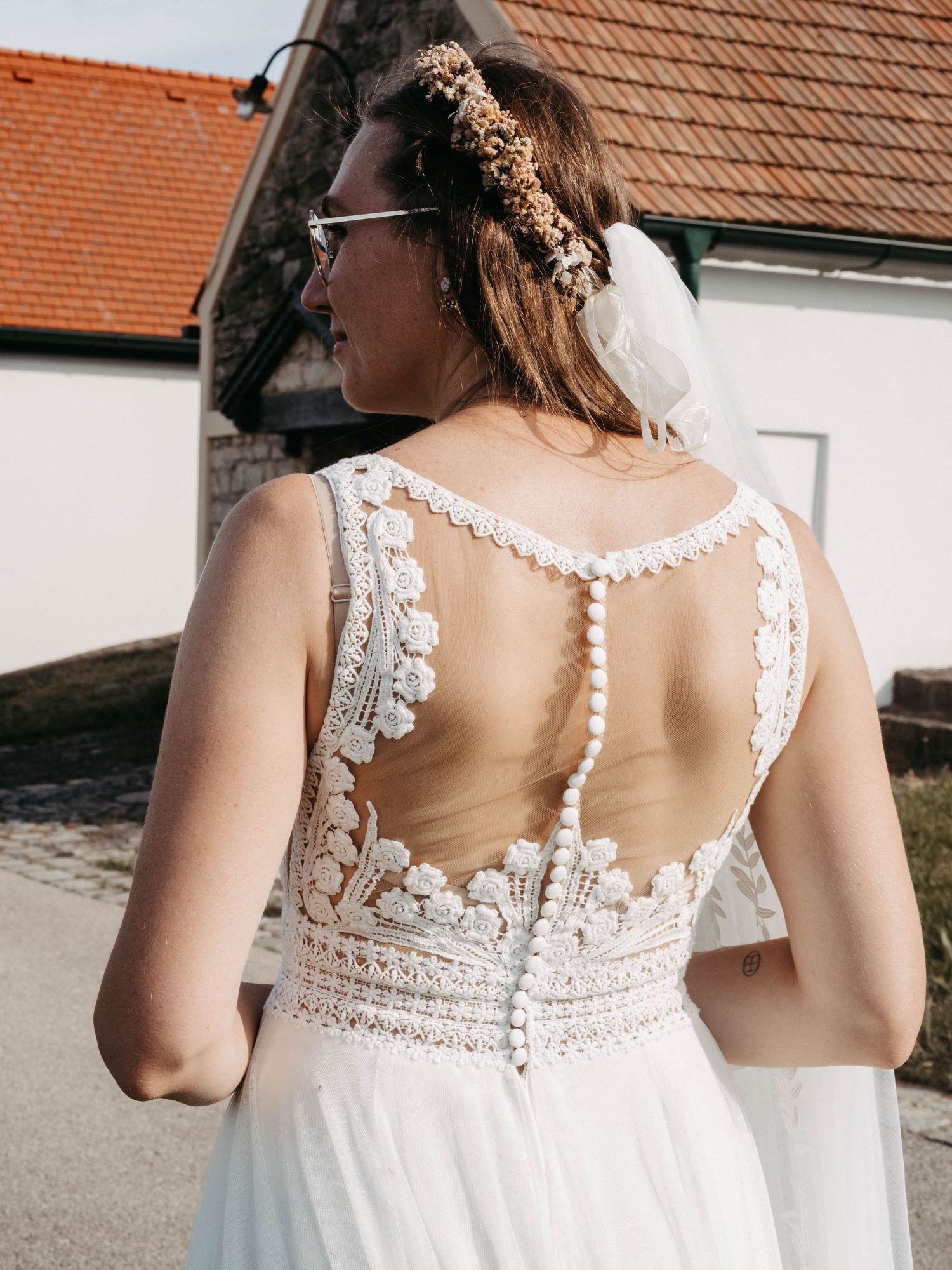Bride in a boho lace wedding dress with button back detail and floral hair accessory, photographed outdoors.