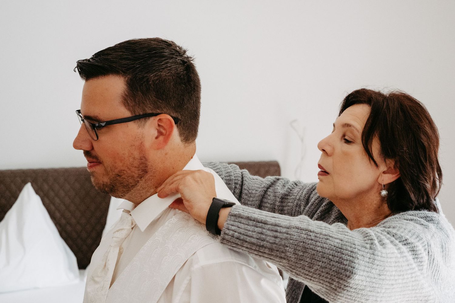 Woman helping man adjust his collar and tie while getting dressed for a formal event.