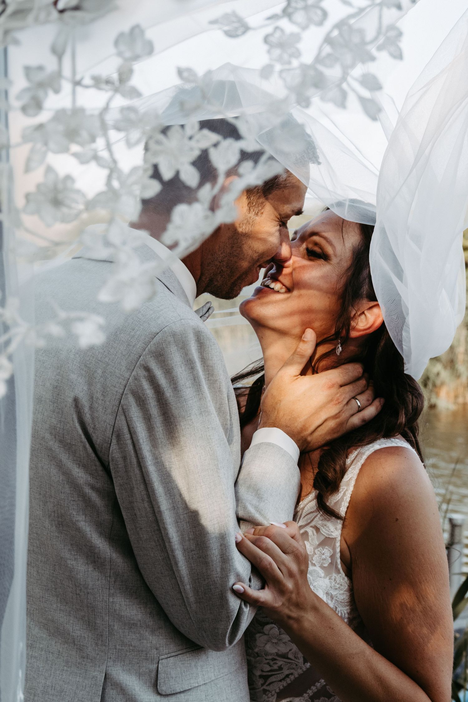 Romantic wedding moment captured through sheer white veil during outdoor ceremony.