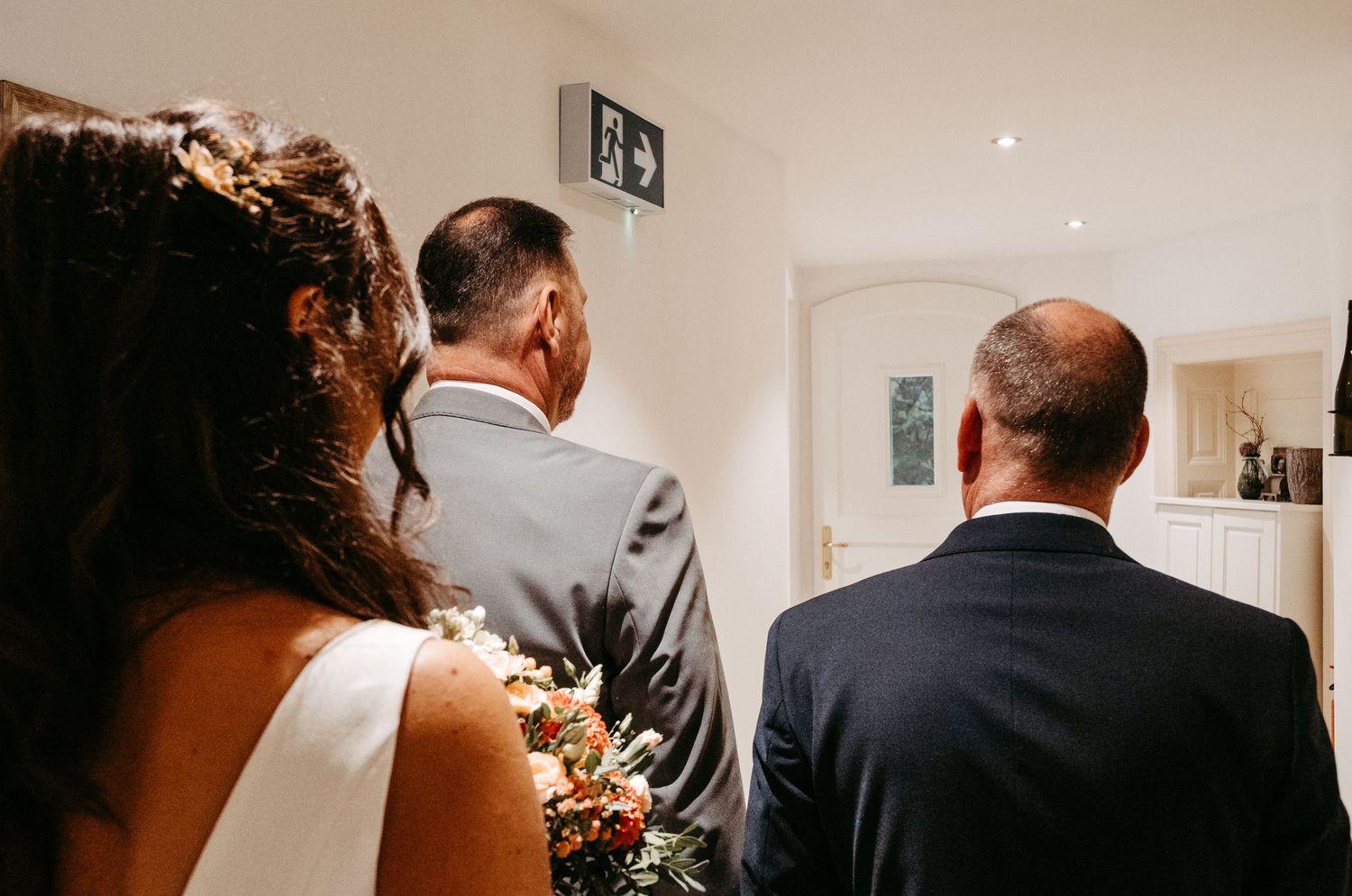 Wedding party walking through doorway during indoor ceremony procession.
