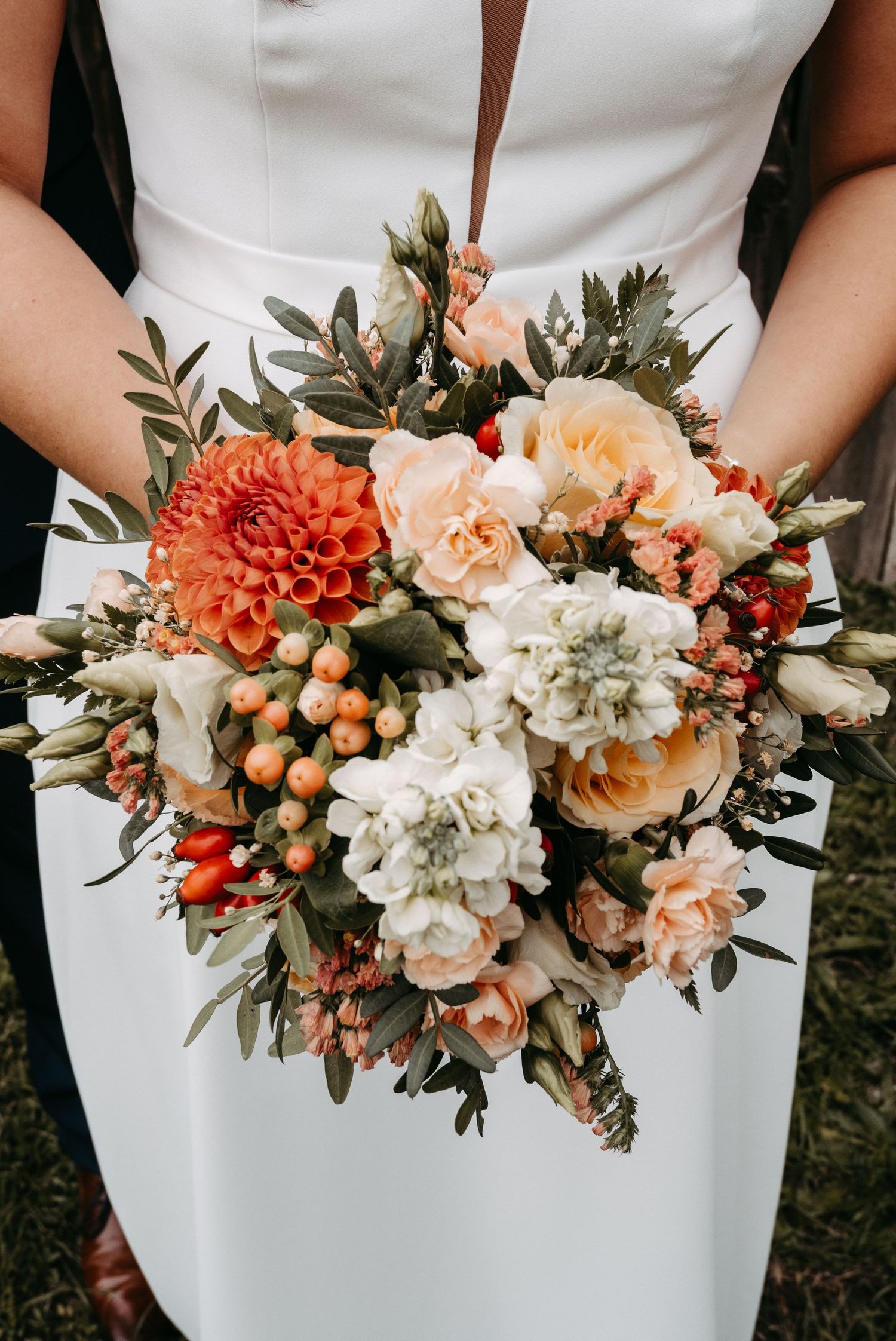 Bride holding lush autumn wedding bouquet with orange dahlias and white flowers.
