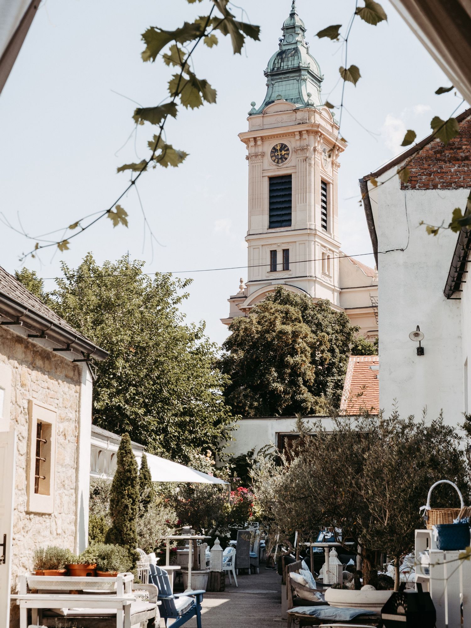 Charming outdoor cafe terrace with white furniture beside a historic baroque church tower in a European village.