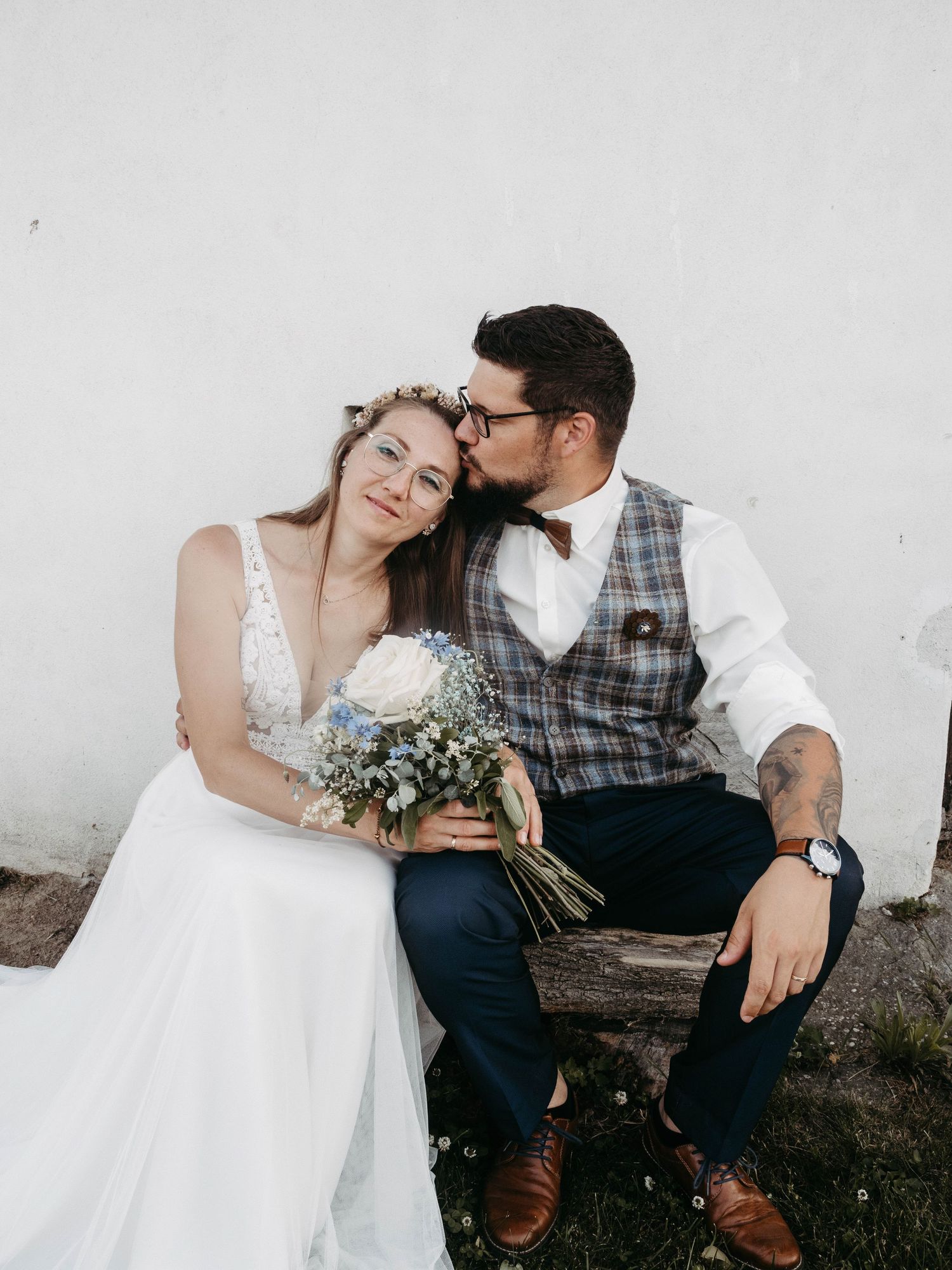 A couple shares intimate moments on a bench in wedding attire.