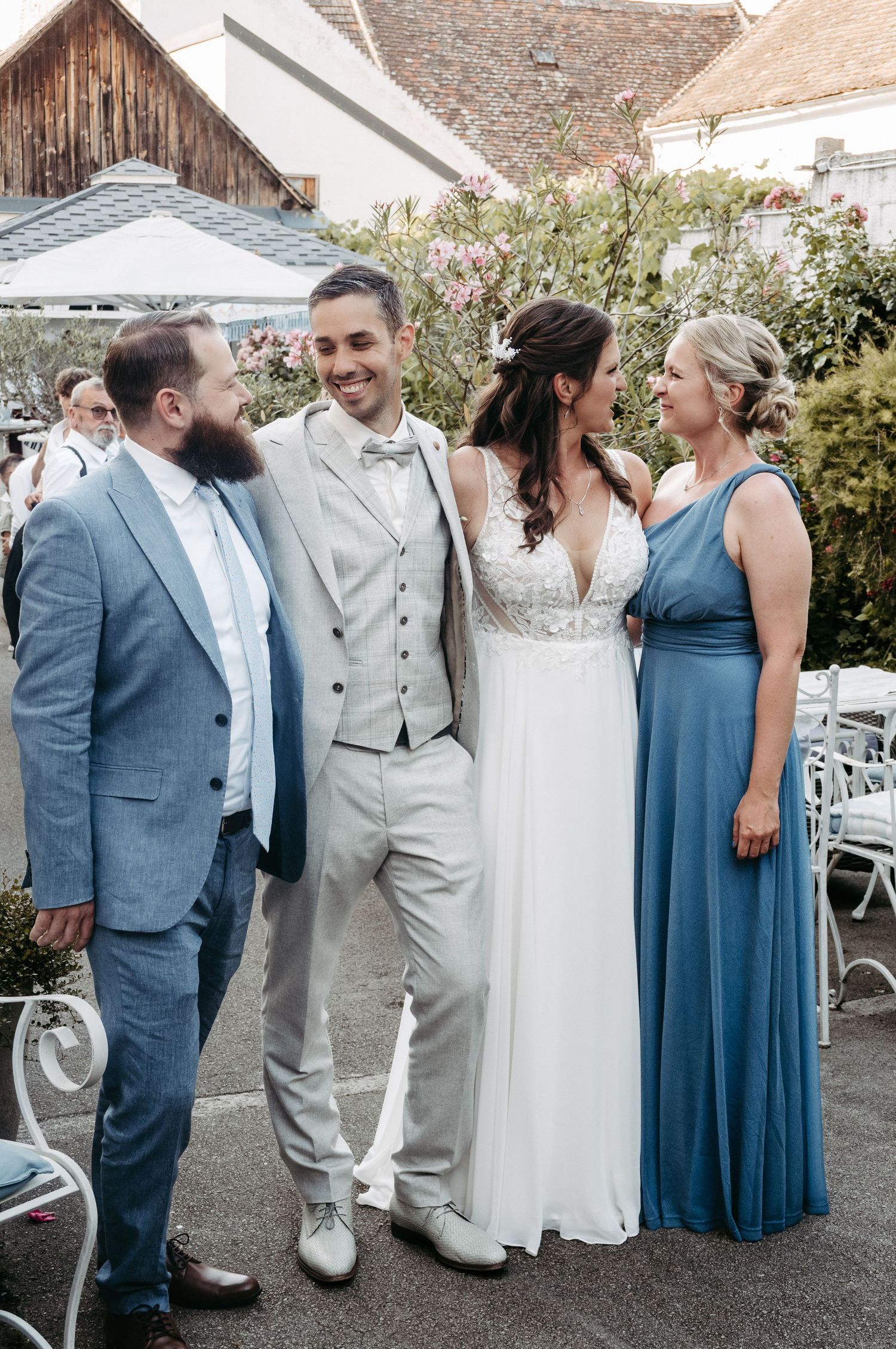 A smiling bride and groom pose with two guests in blue attire at an outdoor wedding reception.