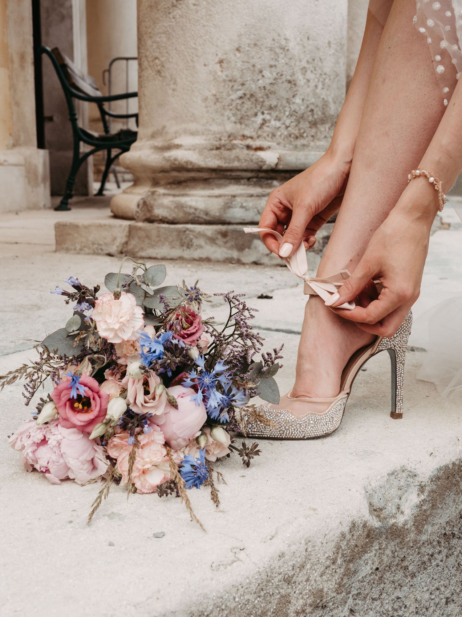 Delicate pink and blue floral arrangement next to bridal shoes on stone steps.