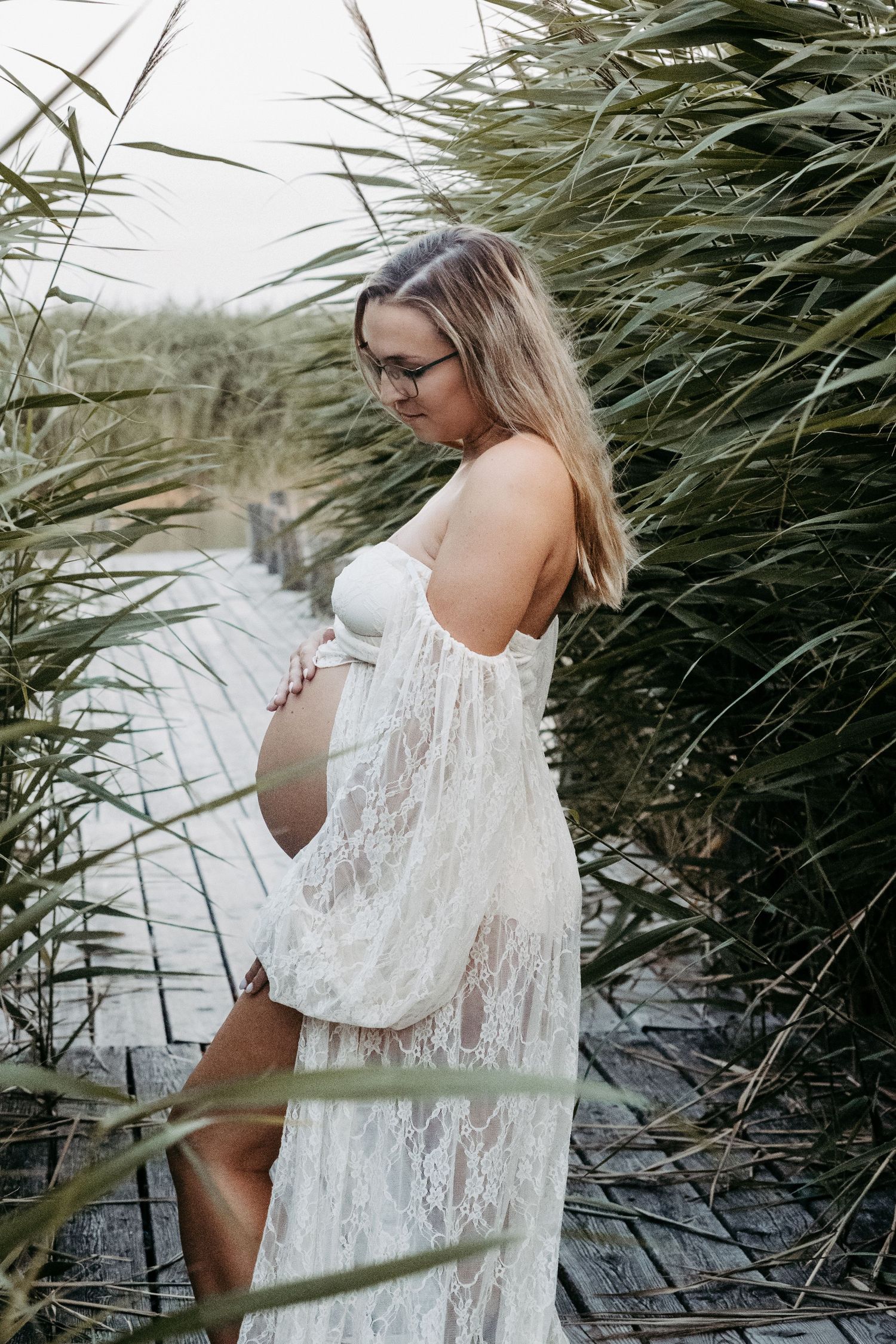 Ethereal photos near lake reeds showing a flowing white lace dress against natural foliage.