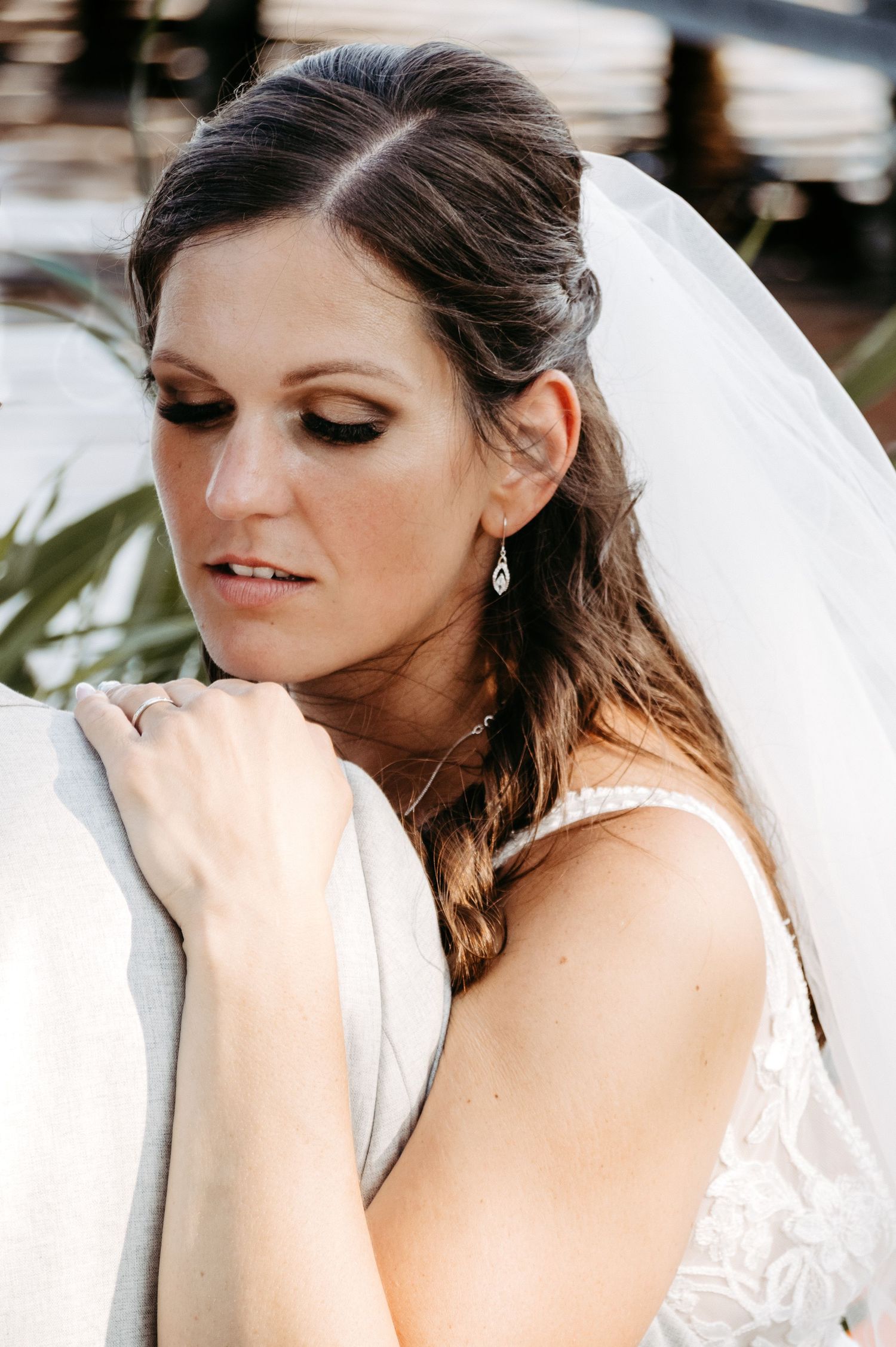 Elegant bride in white lace gown and veil, wearing teardrop earrings, gazes down with smoky eye makeup.