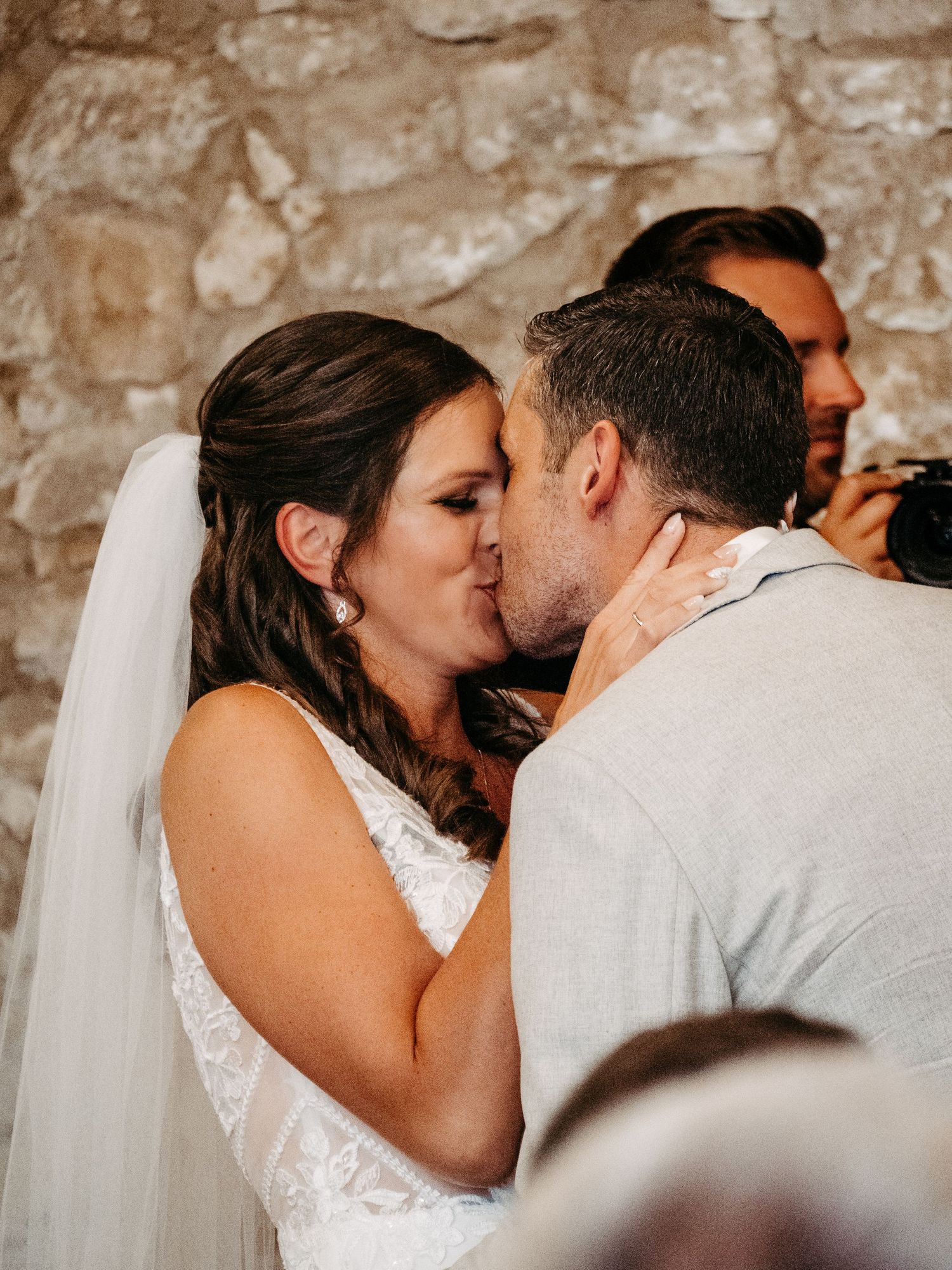 Bride and groom share their first kiss at the altar during a romantic wedding ceremony in a rustic stone venue.