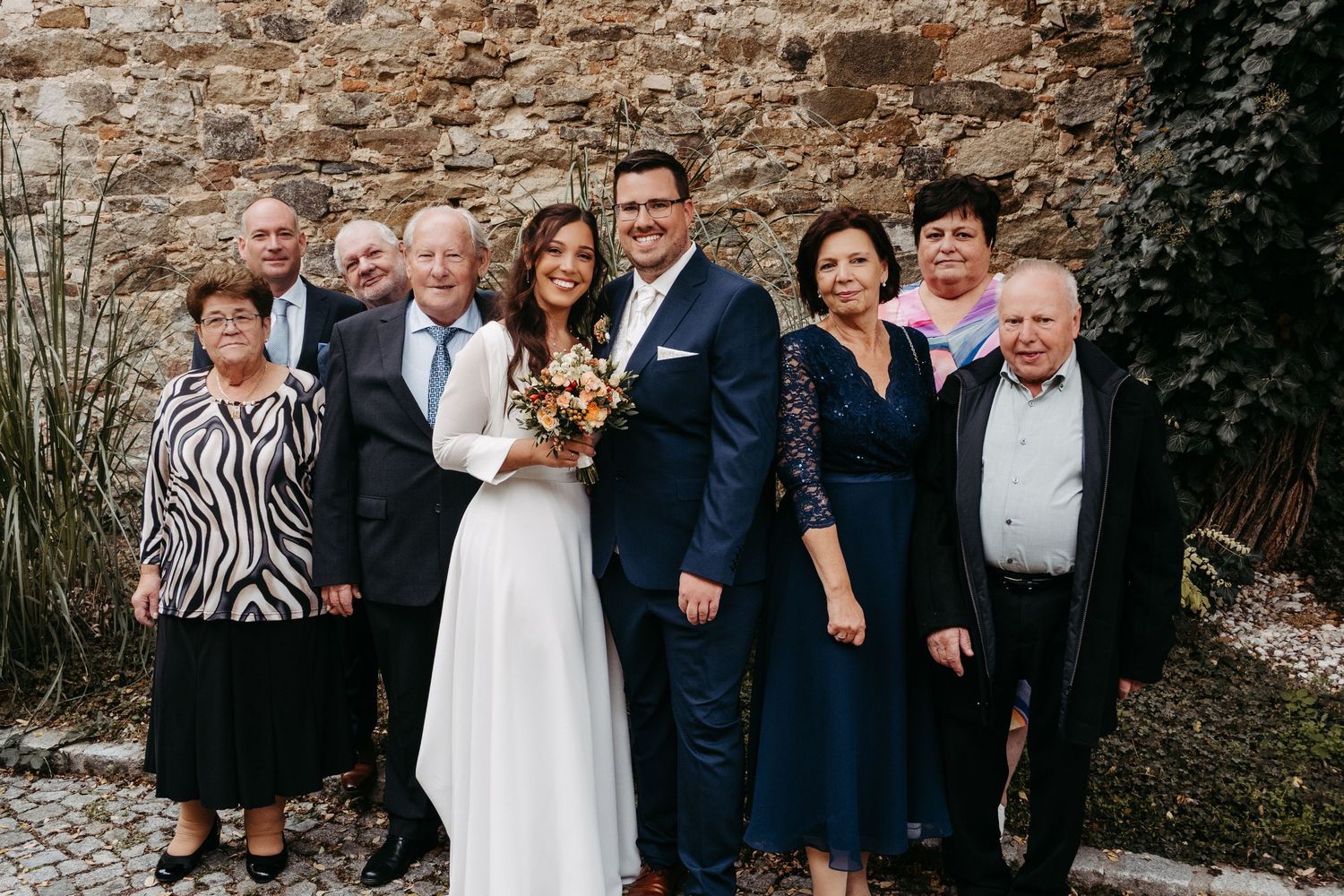 Wedding couple posing with family members in front of rustic stone wall outdoors.