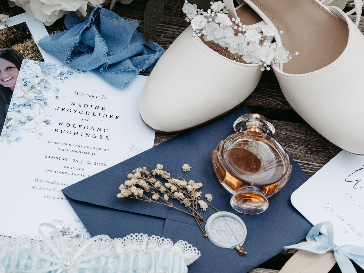 Wedding accessories including blue stationery, jewelry and decorative items on dark surface.