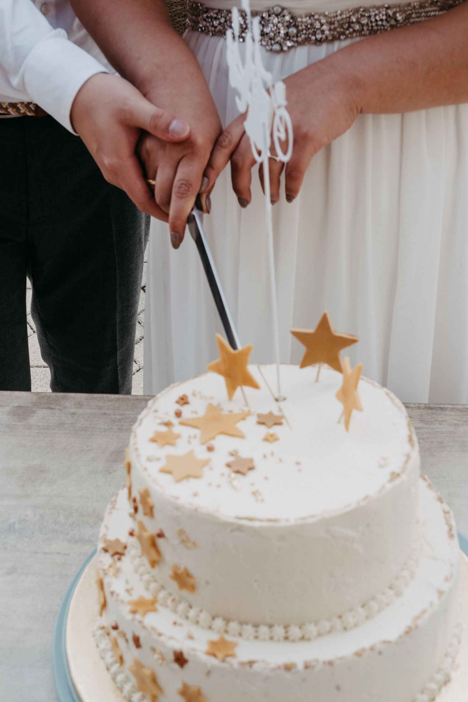 Bride and groom cutting a two-tier white wedding cake decorated with gold stars and star-shaped toppers.