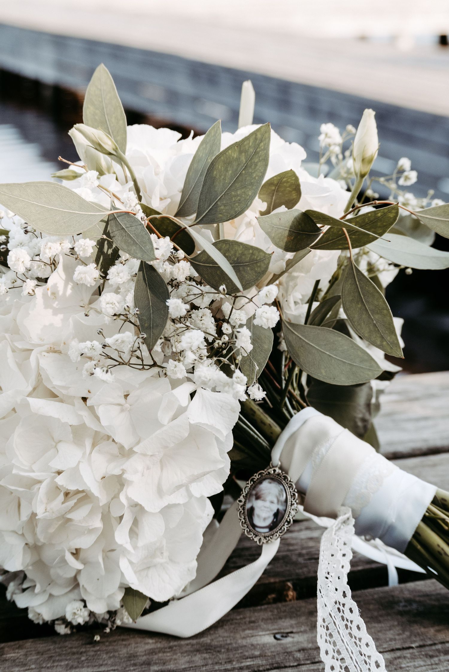 White hydrangea wedding bouquet with eucalyptus, baby's breath, and a memorial photo charm wrapped in satin ribbon.