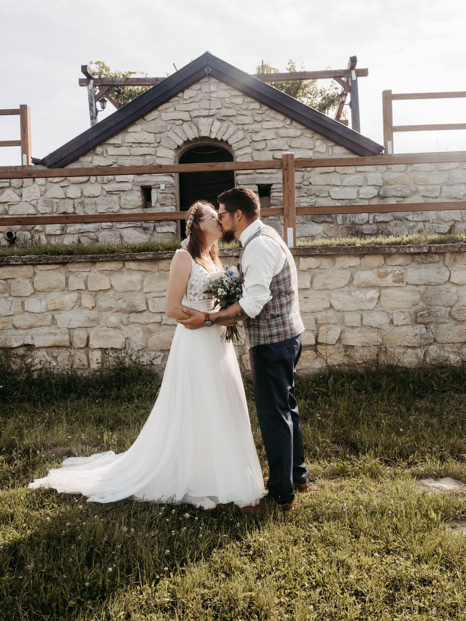 Bride and groom sharing a kiss in front of a rustic stone building on their wedding day.