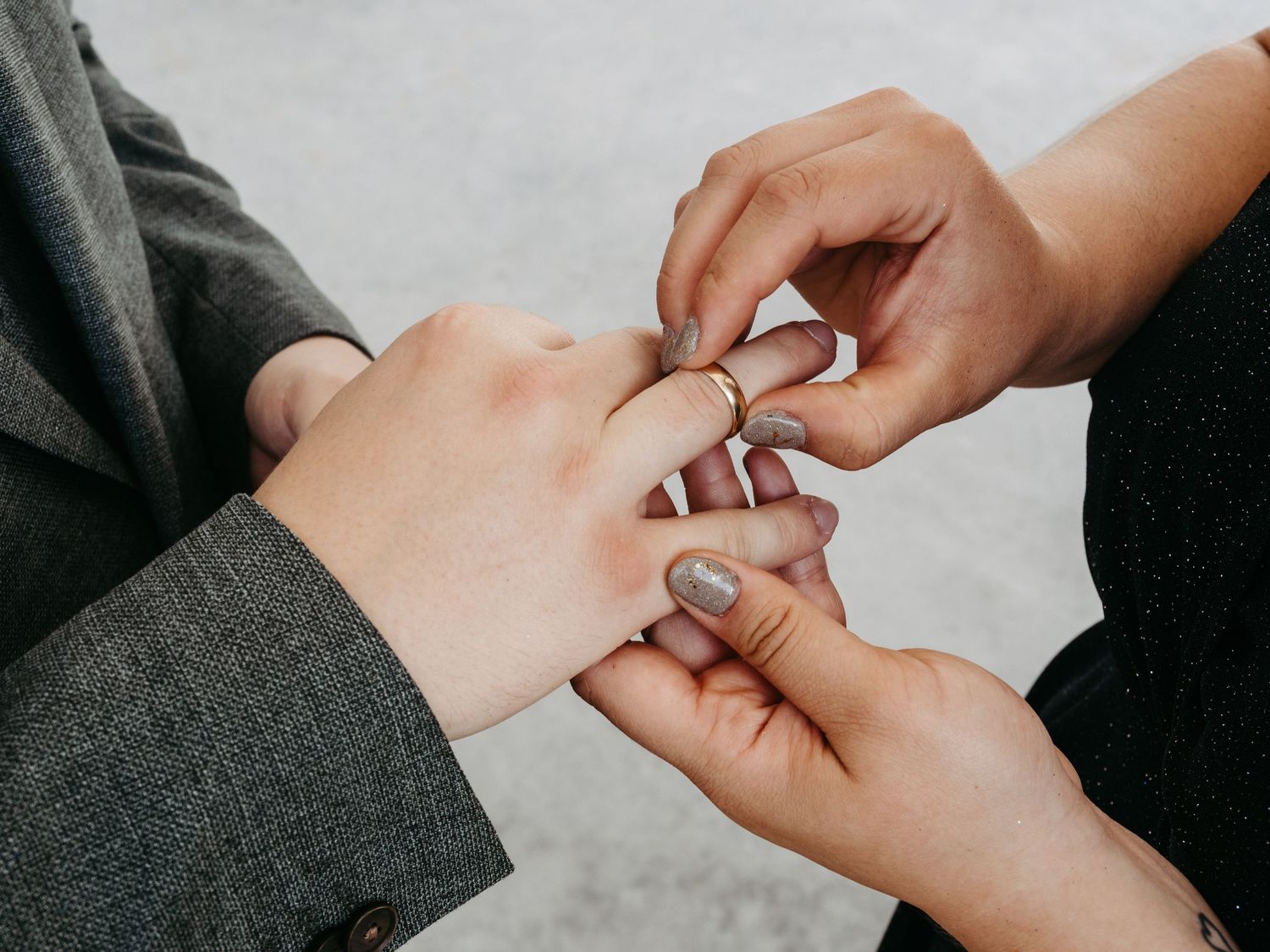 Close-up of hands exchanging a gold wedding ring during a marriage ceremony outdoors.