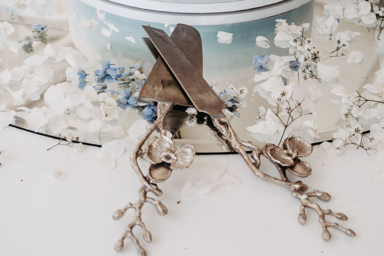 Elegant floral earrings with pearl accents rest beside scissors on a white surface with blue and white flowers.