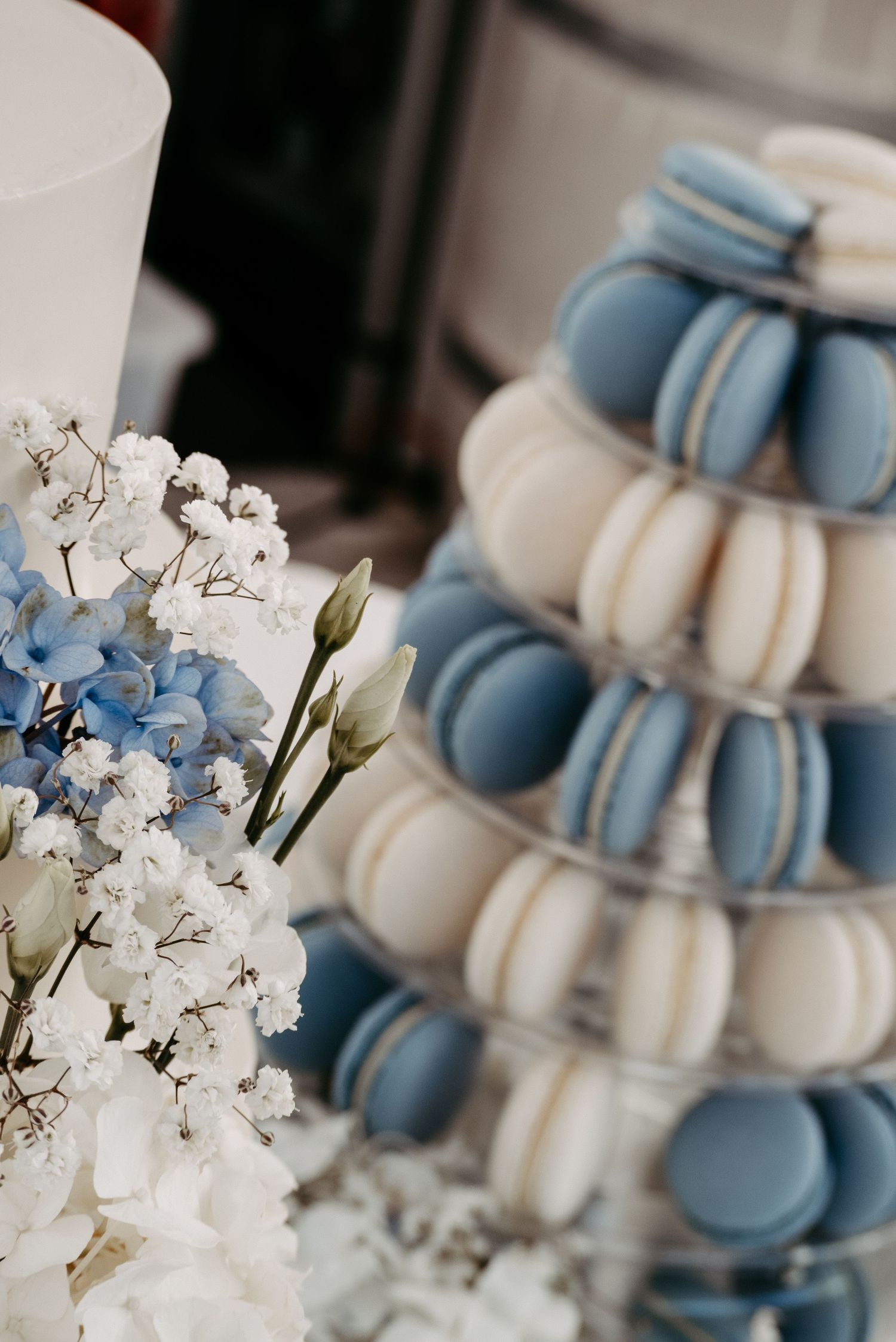 Elegant macaron tower with blue and white macarons beside delicate white and blue flowers at a wedding reception.