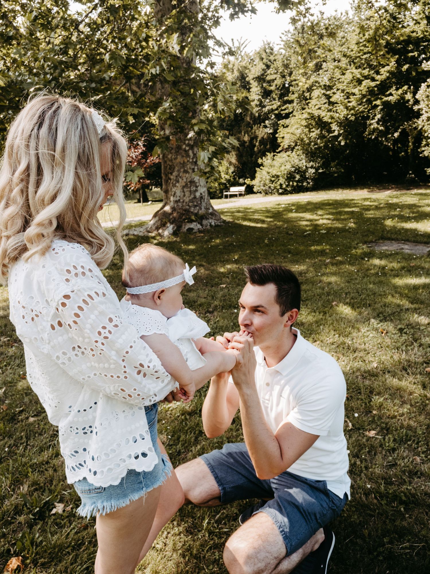 Playful outdoor family photoshoot showing parents interacting with baby in natural setting.