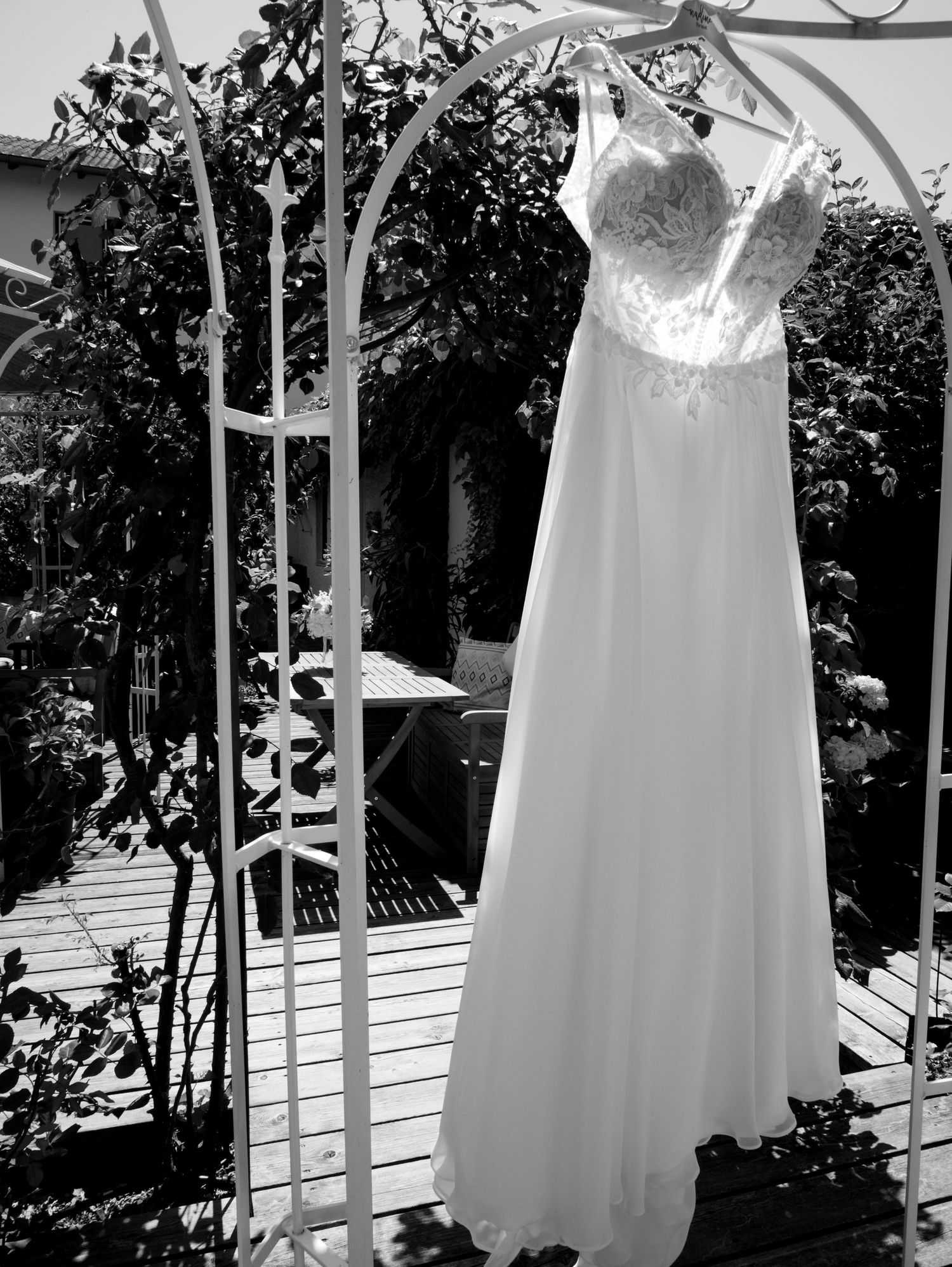 White bridesmaid dresses hanging in a row outdoors against greenery.