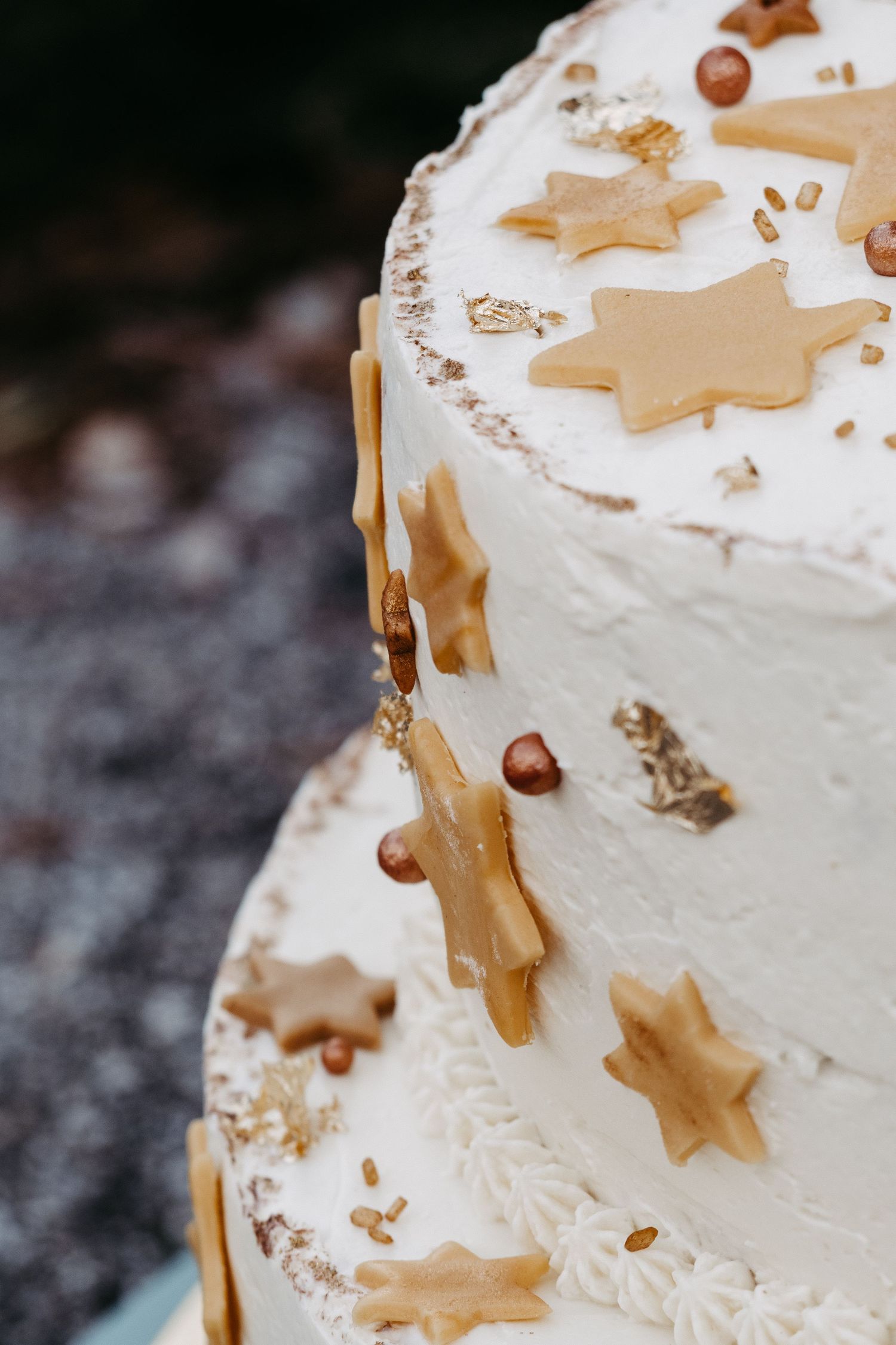 White wedding cake decorated with golden star-shaped cookies, hazelnuts, and gold sprinkles on a two-tier design.