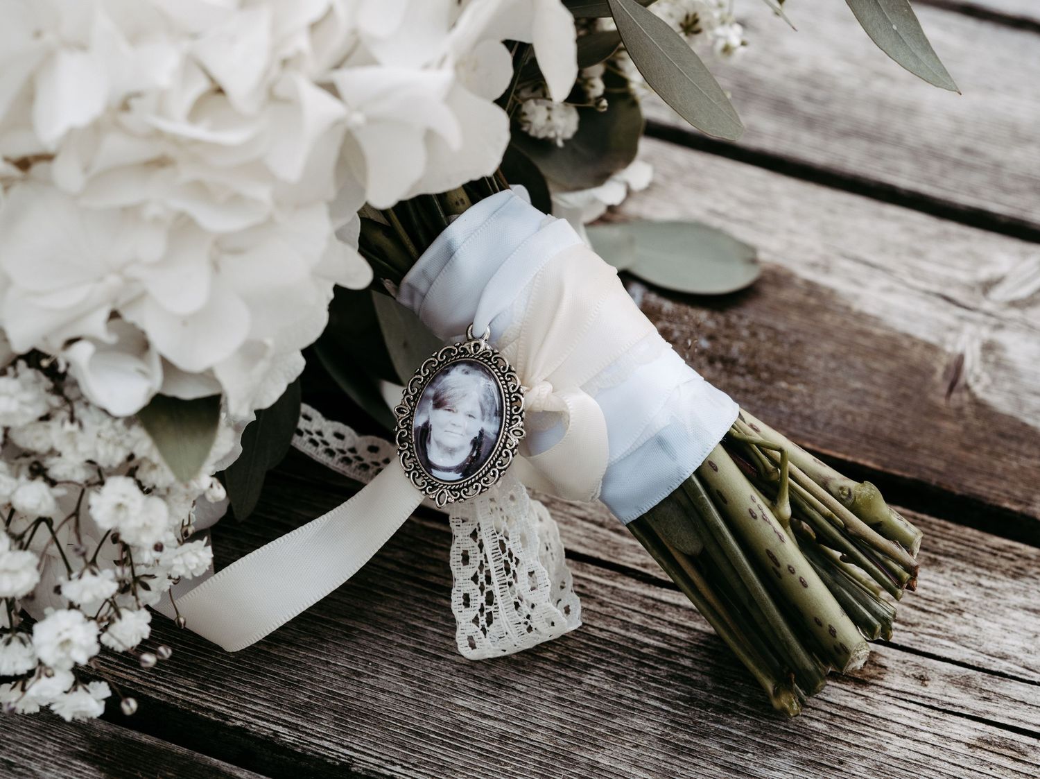 Bridal bouquet of white hydrangeas and baby's breath with a vintage cameo brooch and lace ribbon on rustic wood.