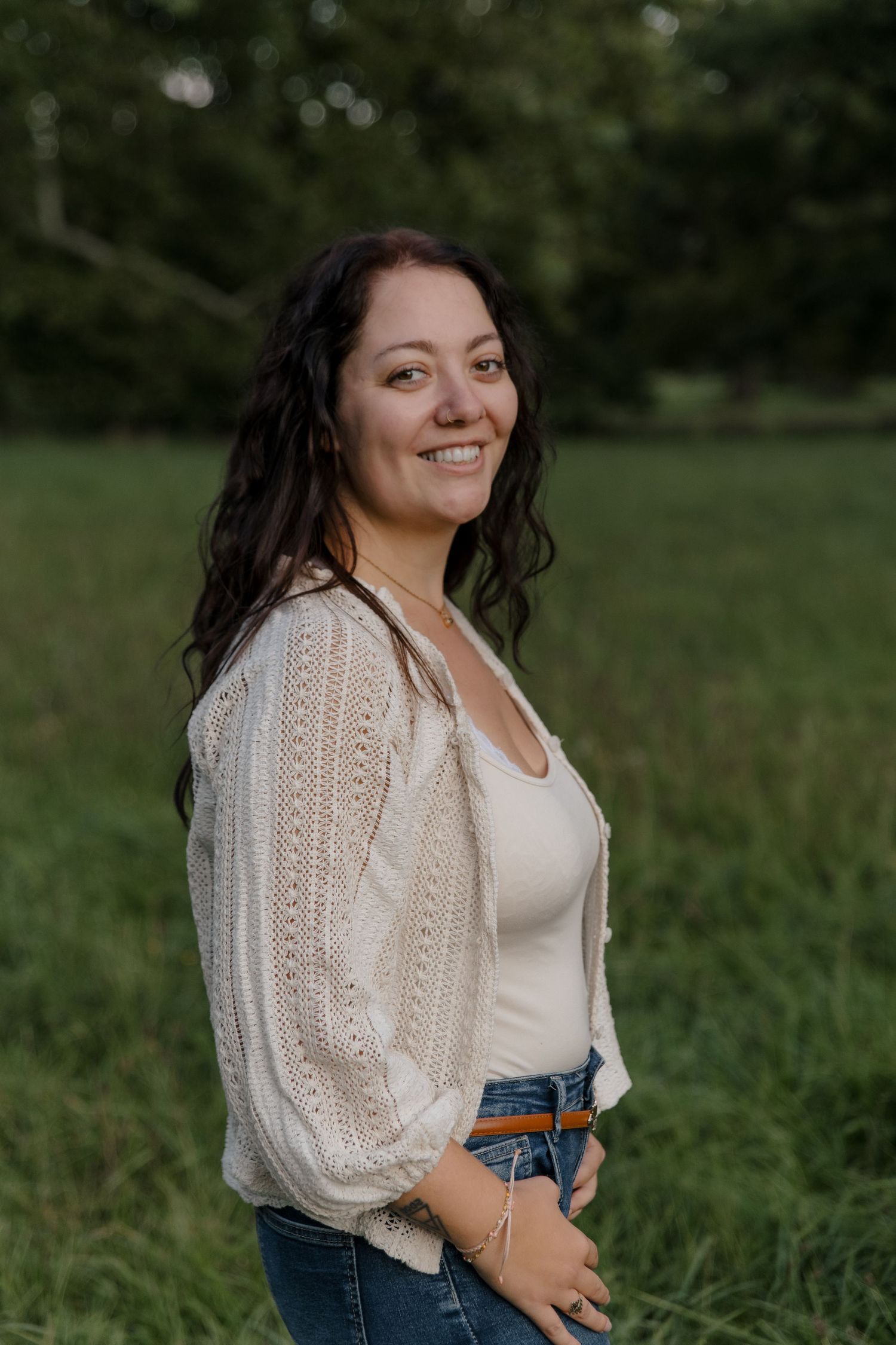 Outdoor portraits in white lace blouse and jeans against natural green background.
