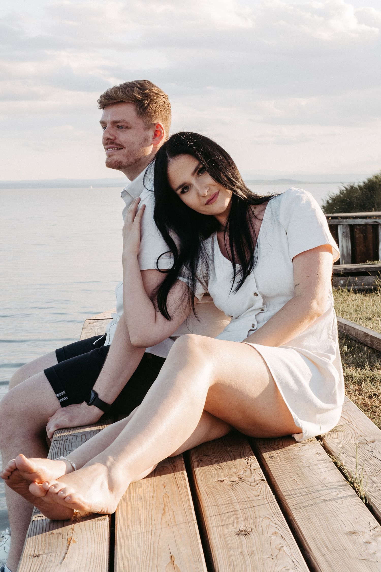 Romantic couple photos on wooden dock by water at sunset.