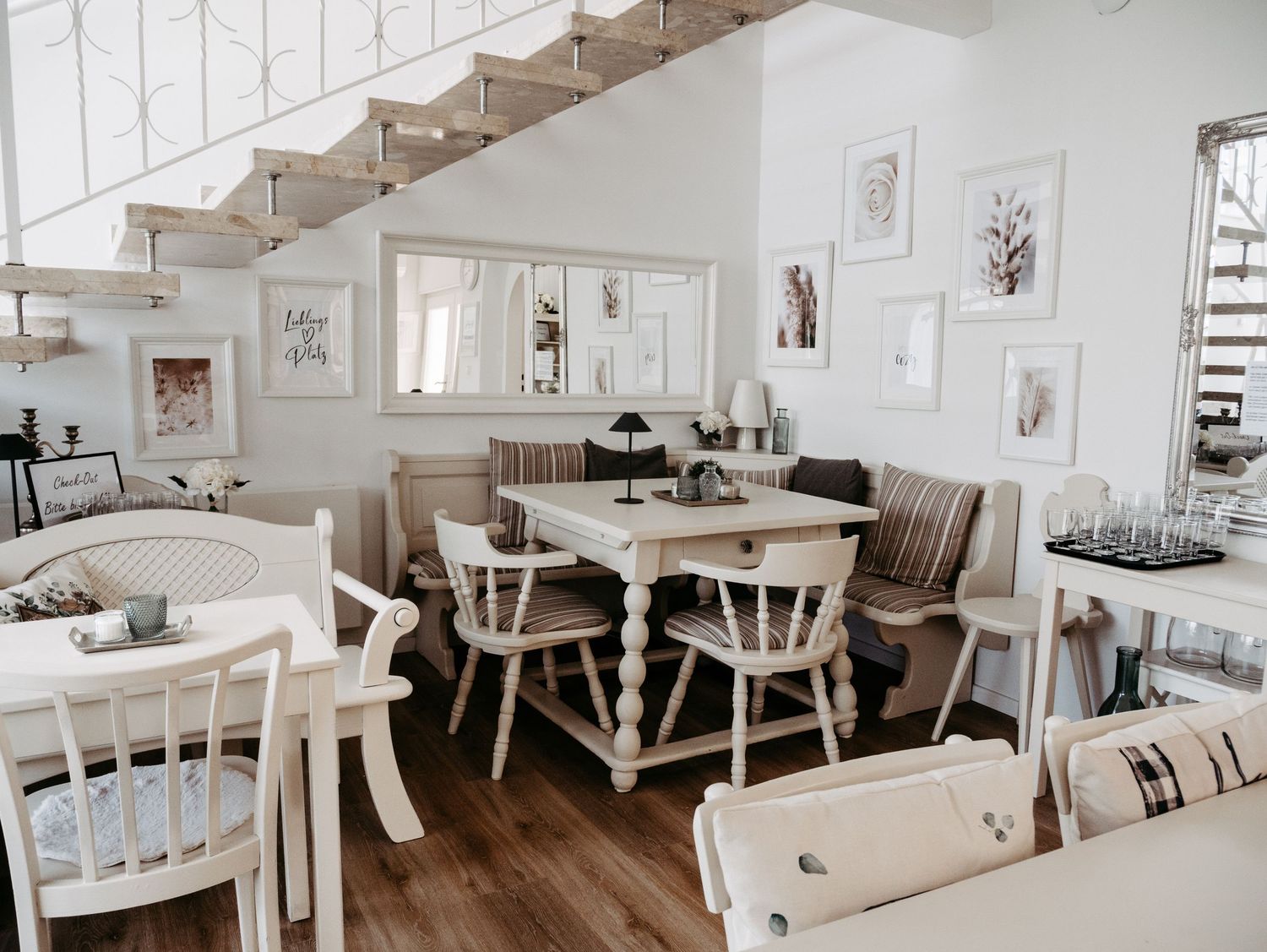 A bright, modern dining space with white furniture and wooden stairs.