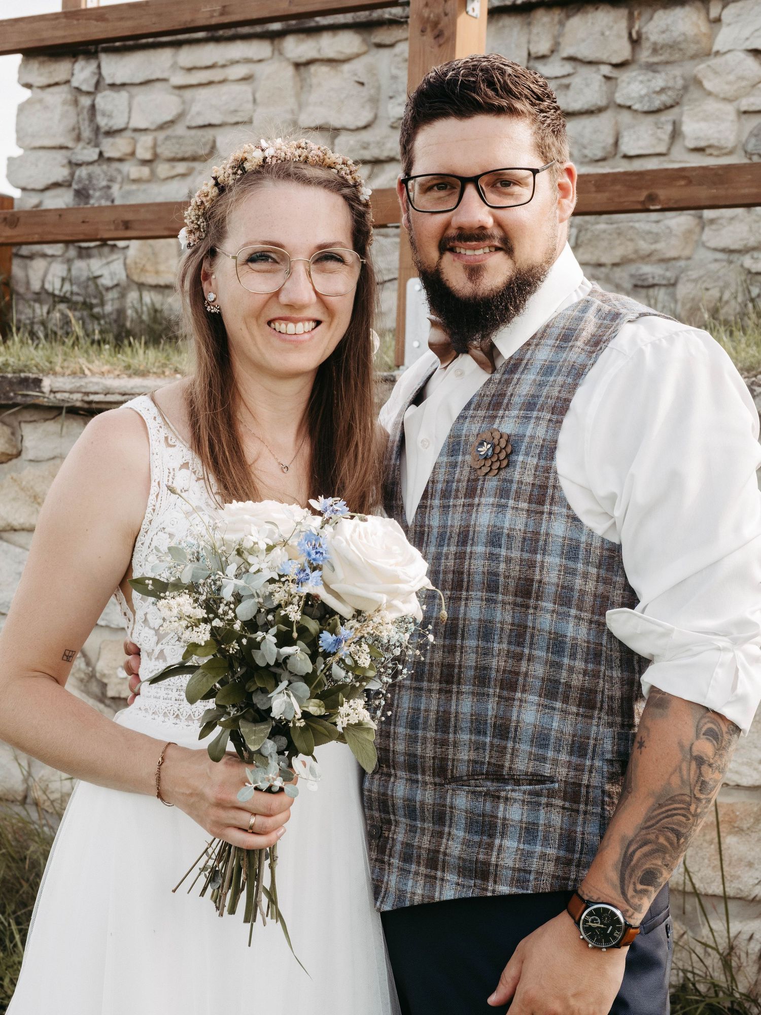 Smiling bride and groom posing together on their wedding day, bride holding blue and white floral bouquet.